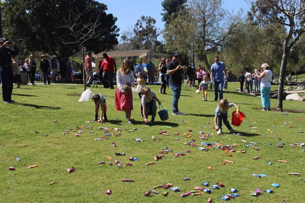 Children and adults searching for Easter eggs on a grassy field during a community event.