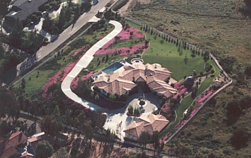 A large residential property with a mansion, swimming pool, and landscaped yard, surrounded by trees and a fence.