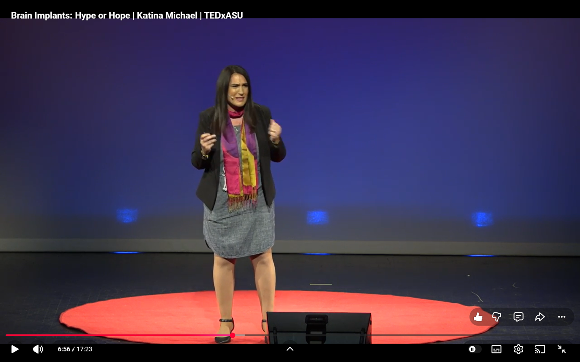 Katina standing on a red circular stage delivering a TEDx talk at Gammage at Tempe, Arizona with a dark blue background.