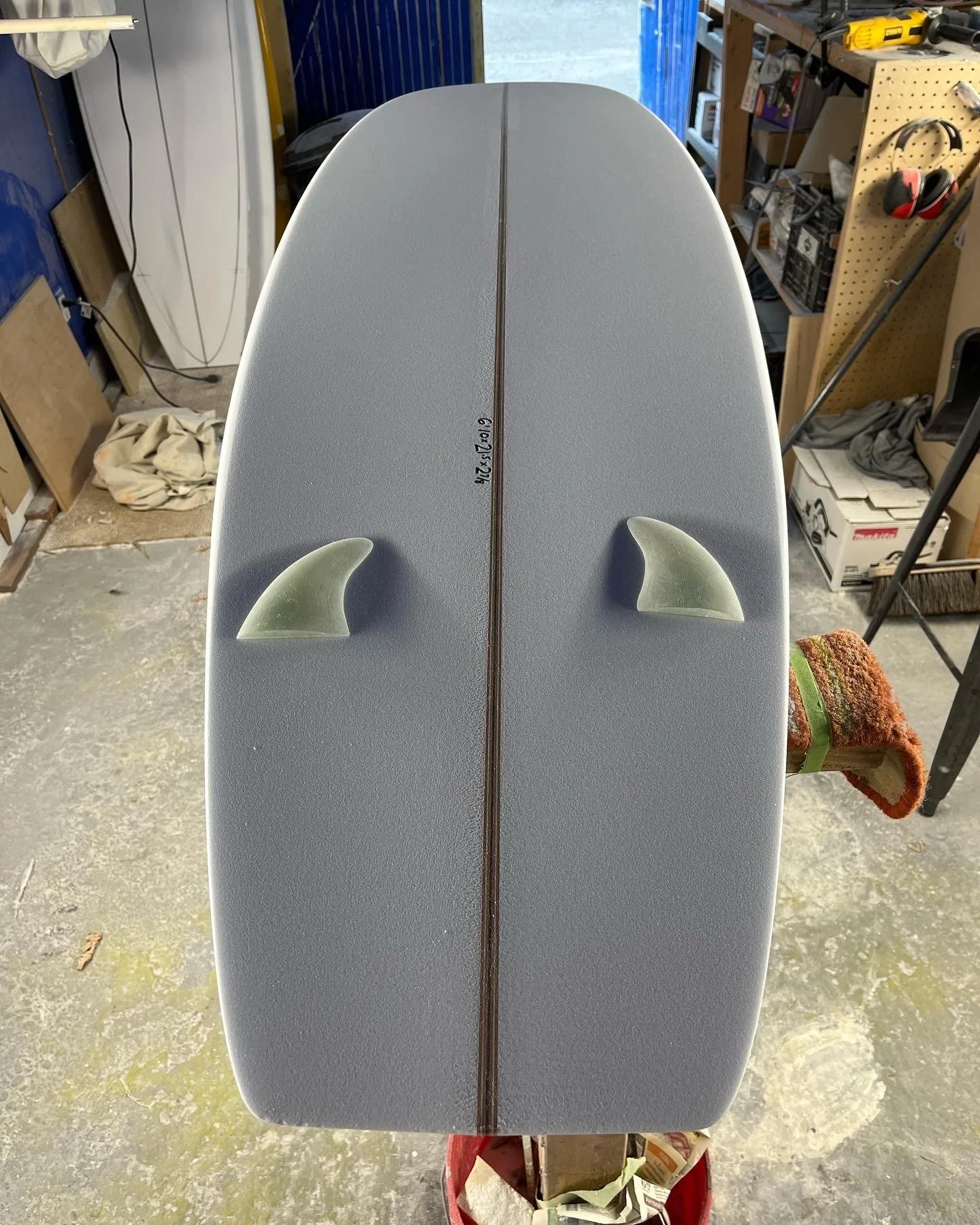 A surfboard with two fins on top, positioned vertically in a garage or workshop setting.