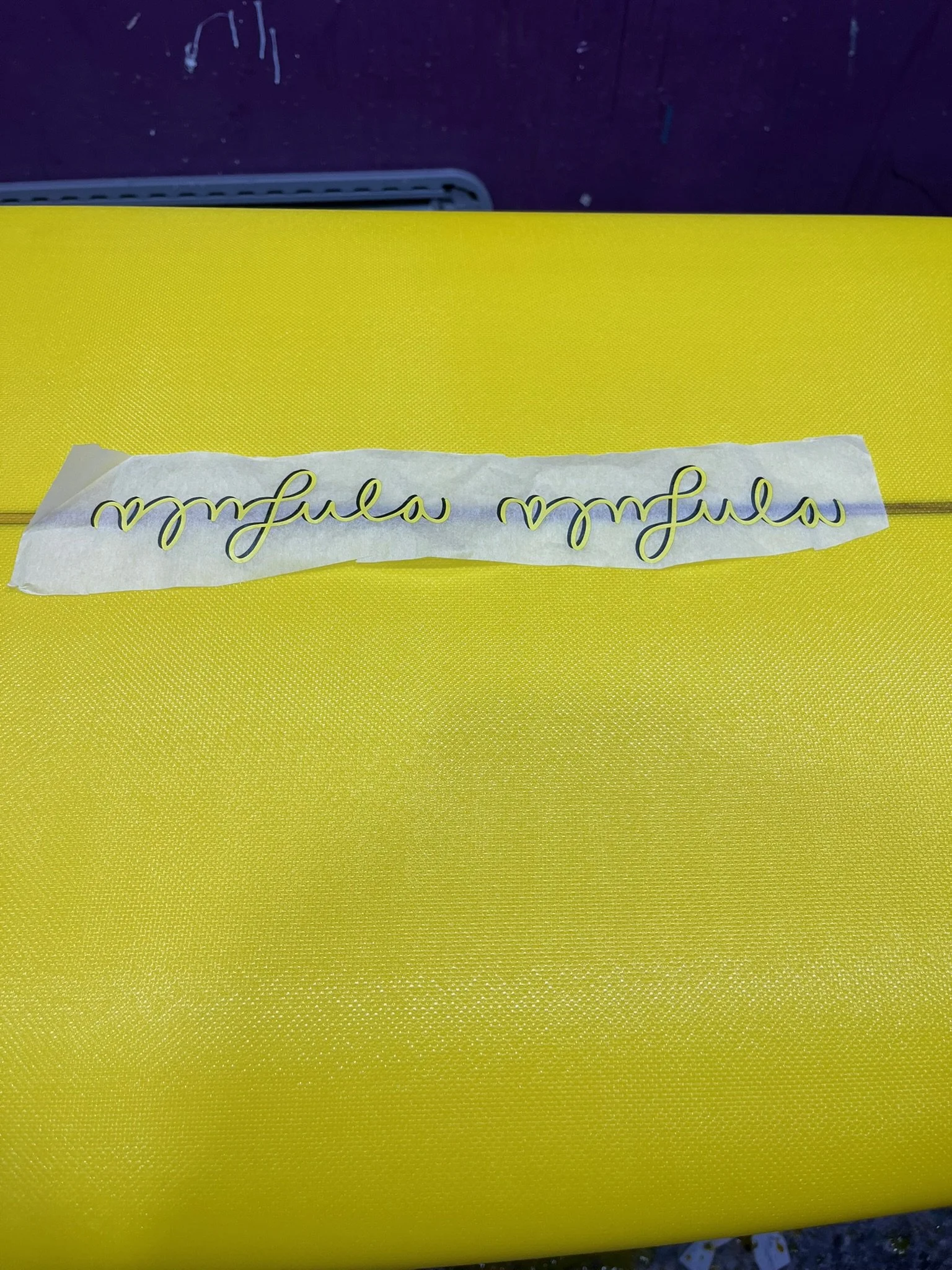 Close-up of yellow textured surface with a piece of white tape that has cursive black and yellow writing on it.