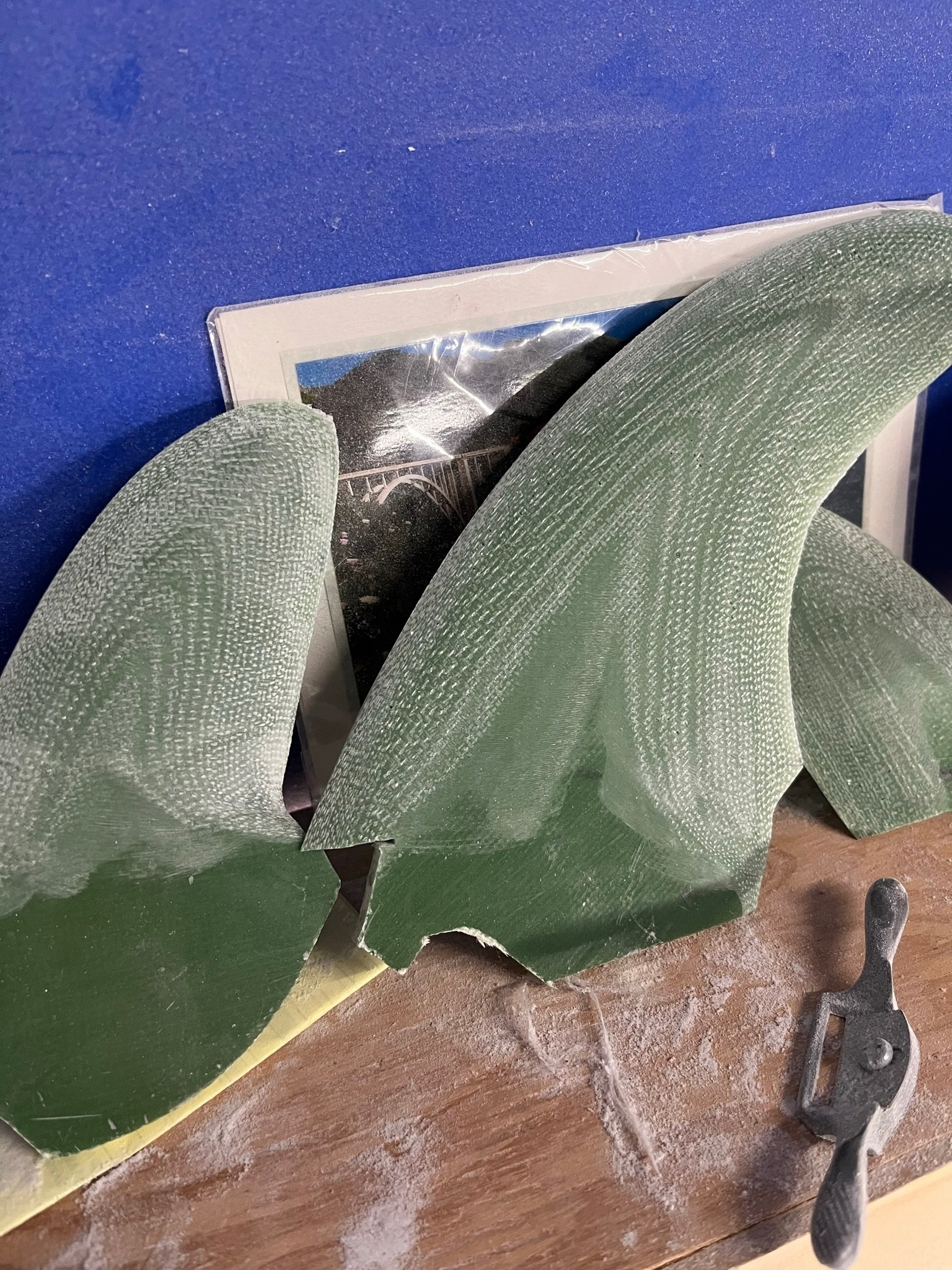 Green glass sheet, a hand covered with a glove, and a sander tool on a wooden surface.