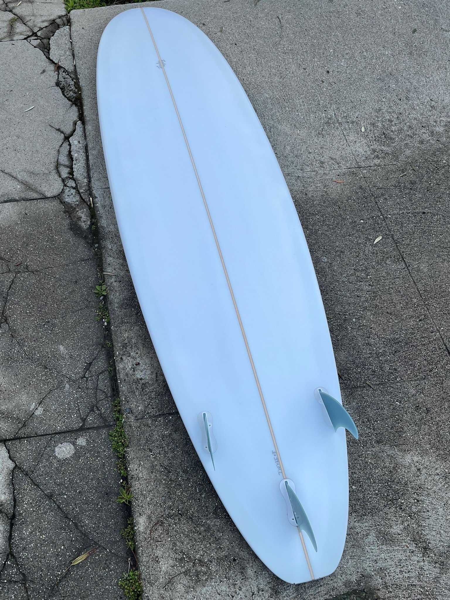 A white surfboard lying on a cracked concrete sidewalk with small green plants growing in the cracks.