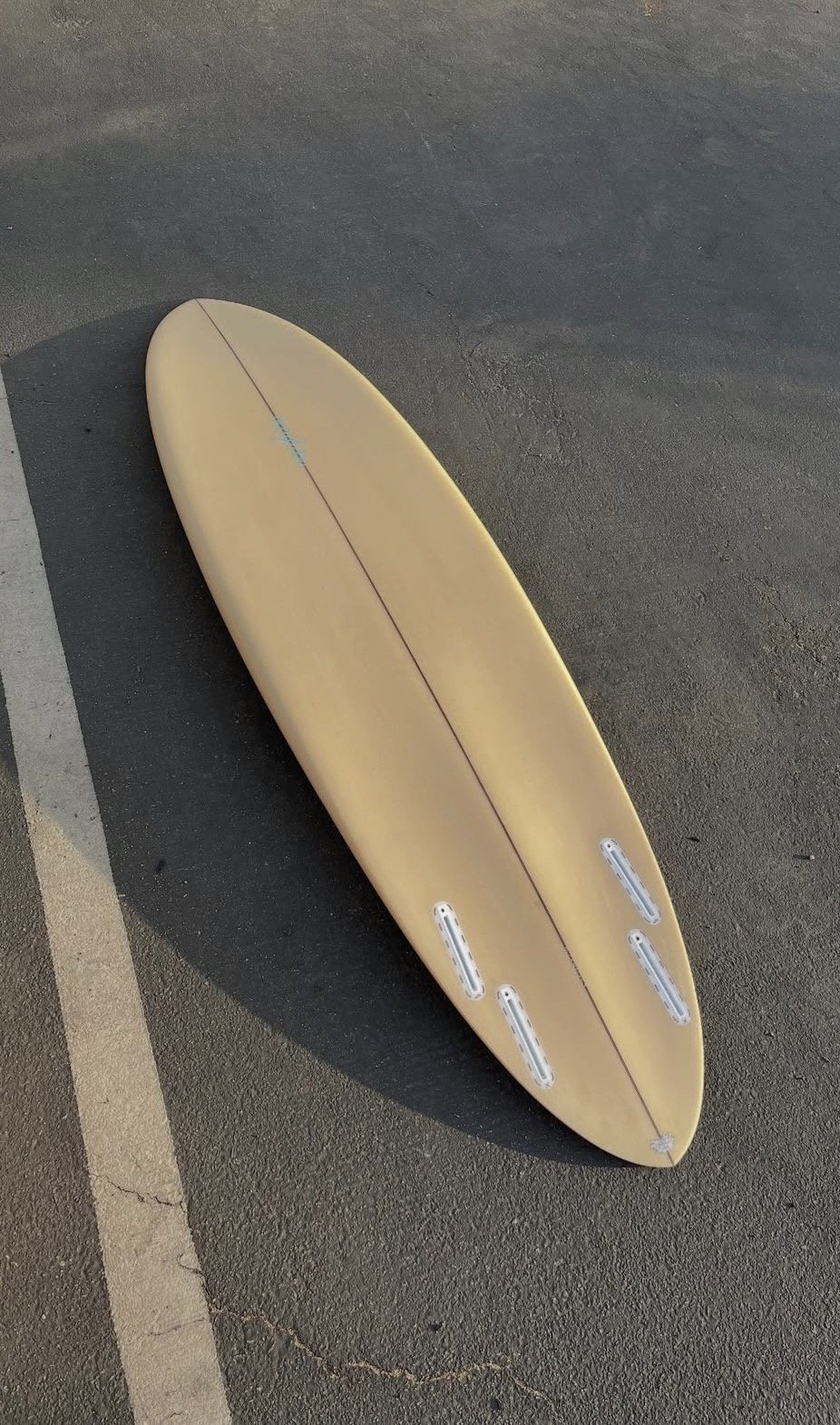 A yellow surfboard lying on the pavement in a parking lot.