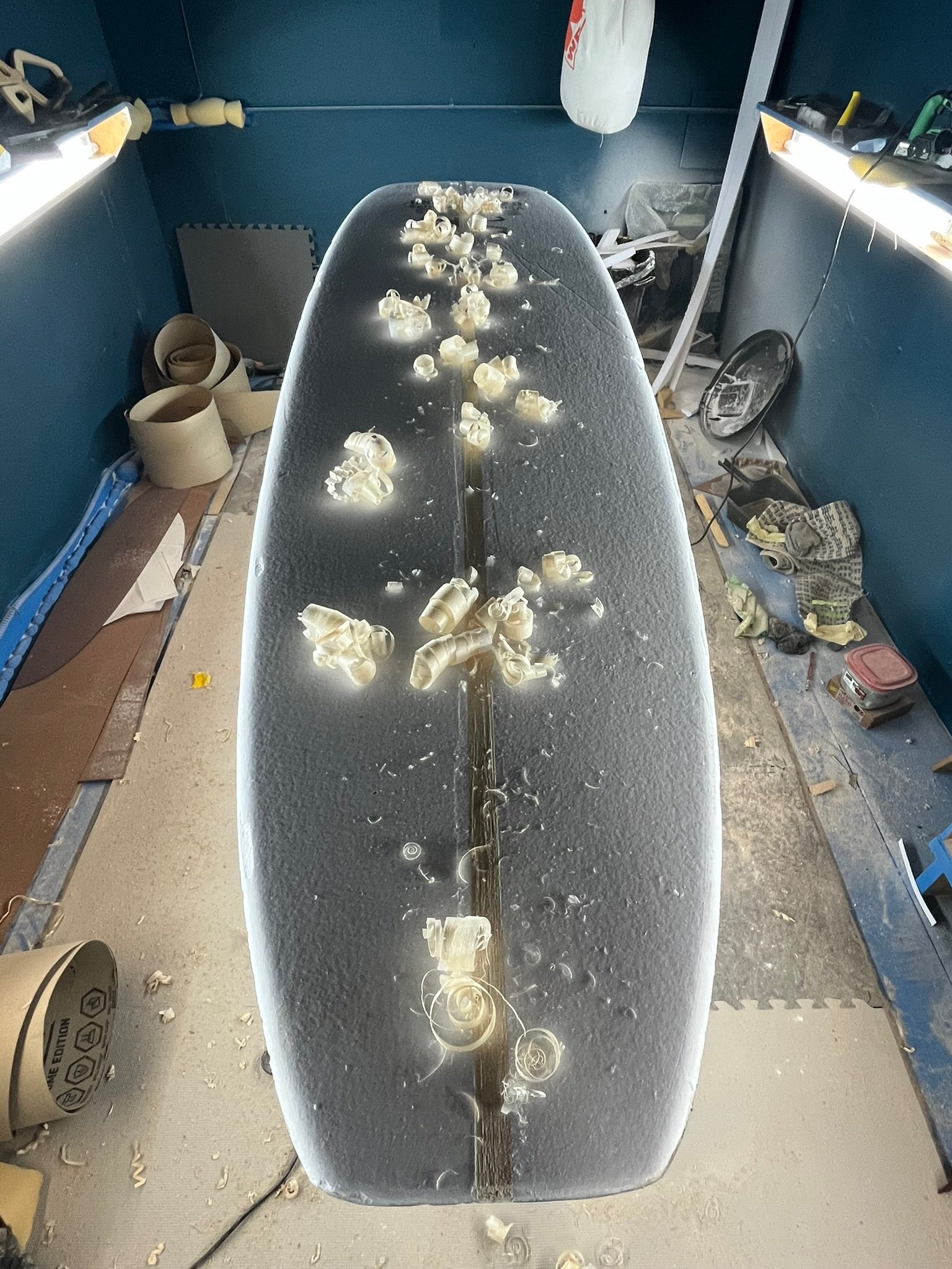 A construction or workshop space with a table covered in plastic shavings, surrounded by tools and materials in a cluttered environment.