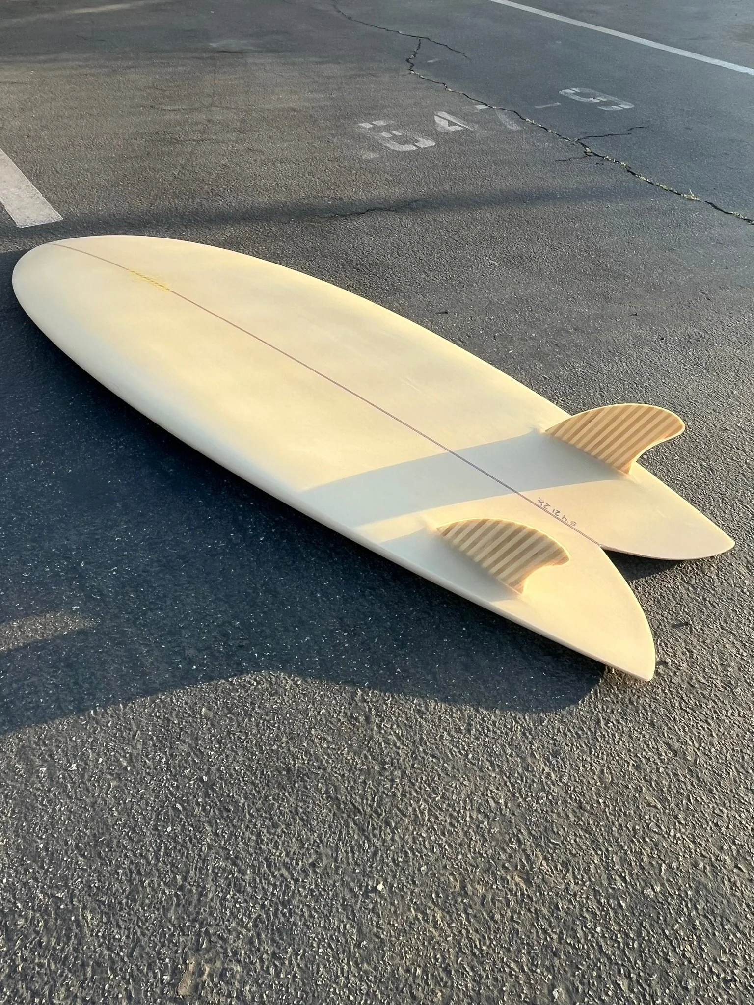 A white surfboard lying on asphalt with a cracking parking lot and faint parking space numbers in the background.