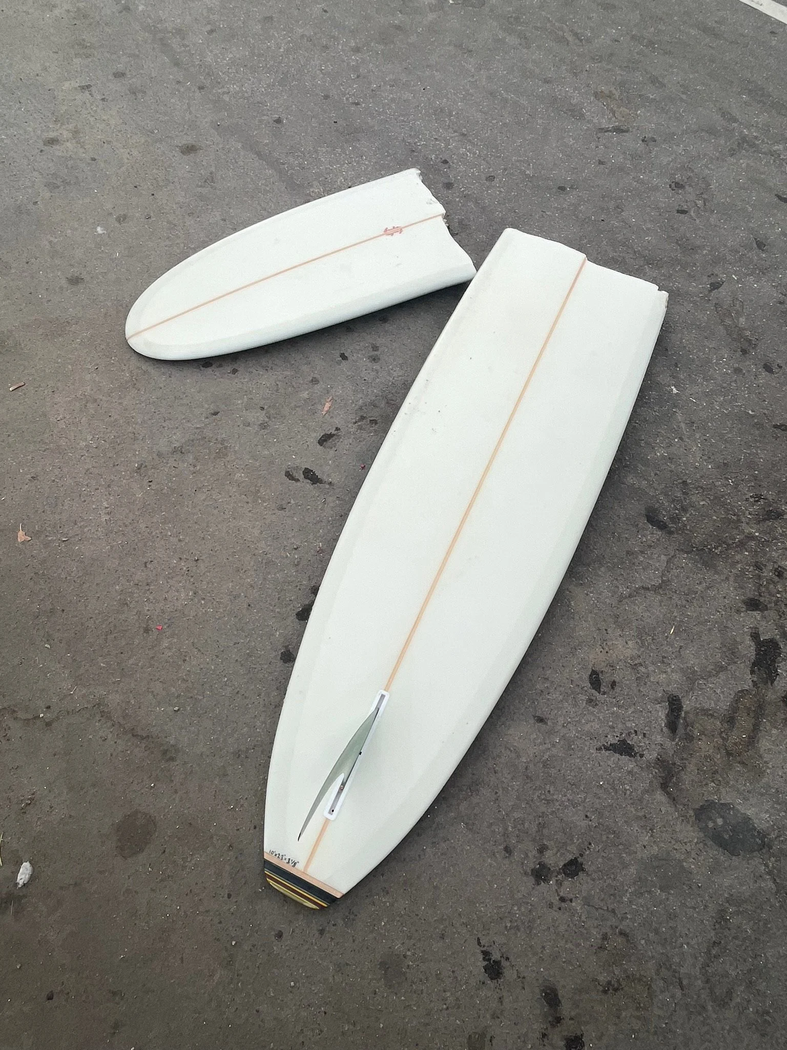 Surfboard and fin lying on a concrete ground.
