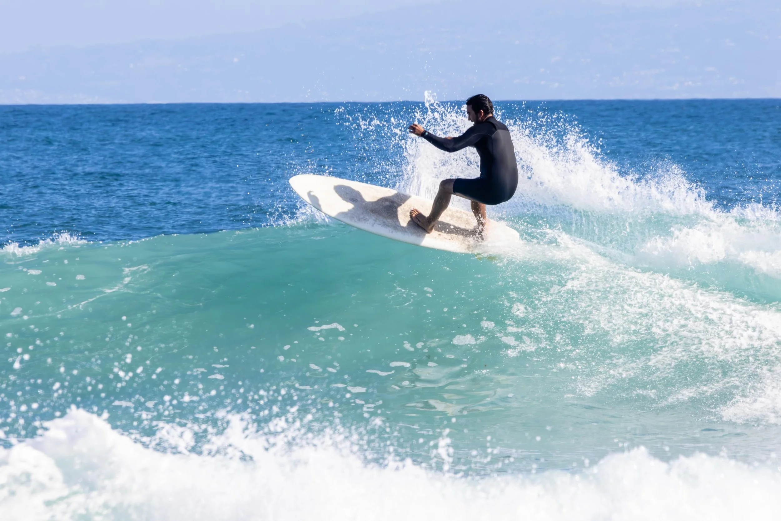 A man riding a surfboard on the ocean waves during the daytime, wearing a black wetsuit.