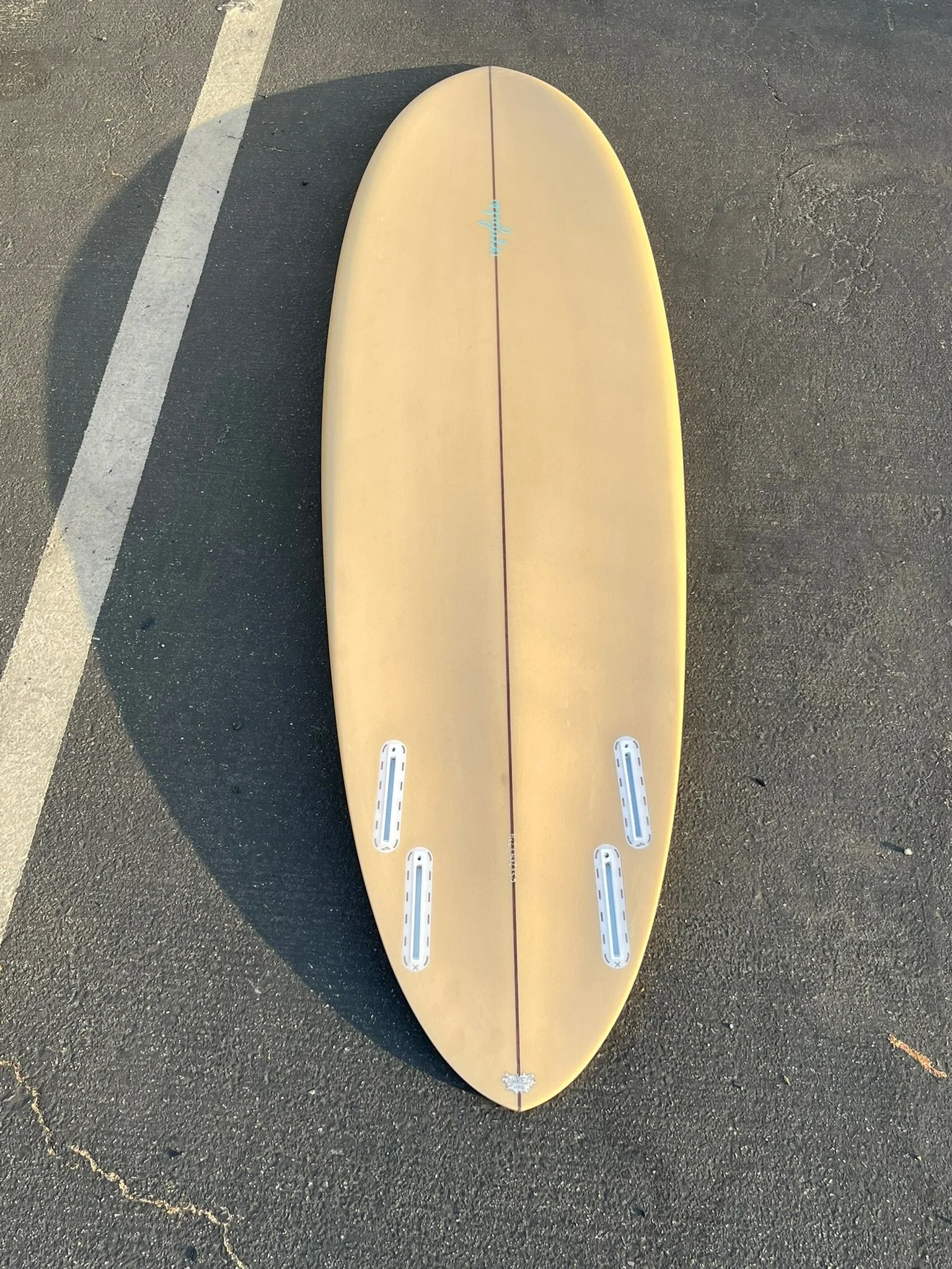 A yellow surfboard lying on a parking lot with a white line and shadows.