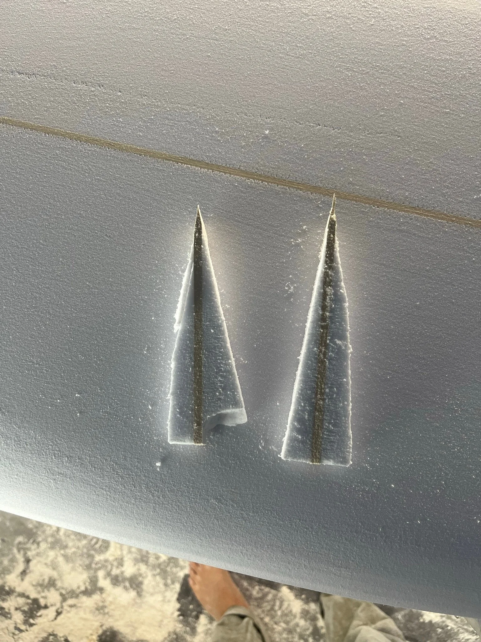 Two foam pieces with sharp points resting on a textured surface, with a person's legs and shoes visible at the bottom of the image.