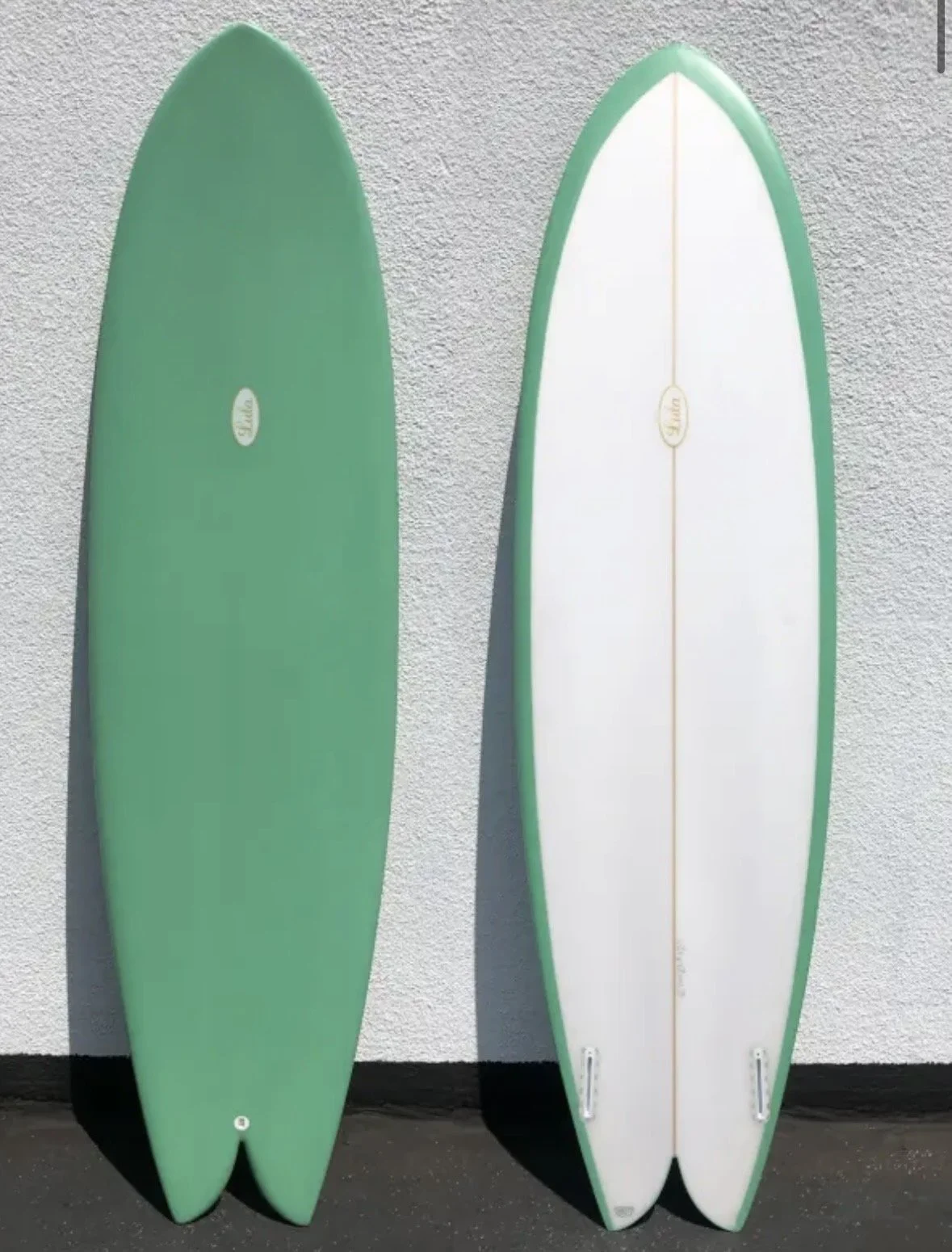 Two surfboards standing upright against a textured wall, one green and the other white with green edges.