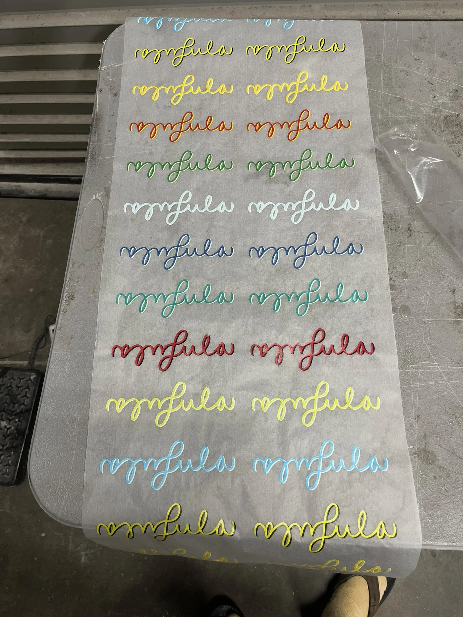Sheet of colorful wire cursive script words in yellow, blue, green, red, light blue, and yellow on baking parchment paper on a work table. Surfboard Laminate paper.