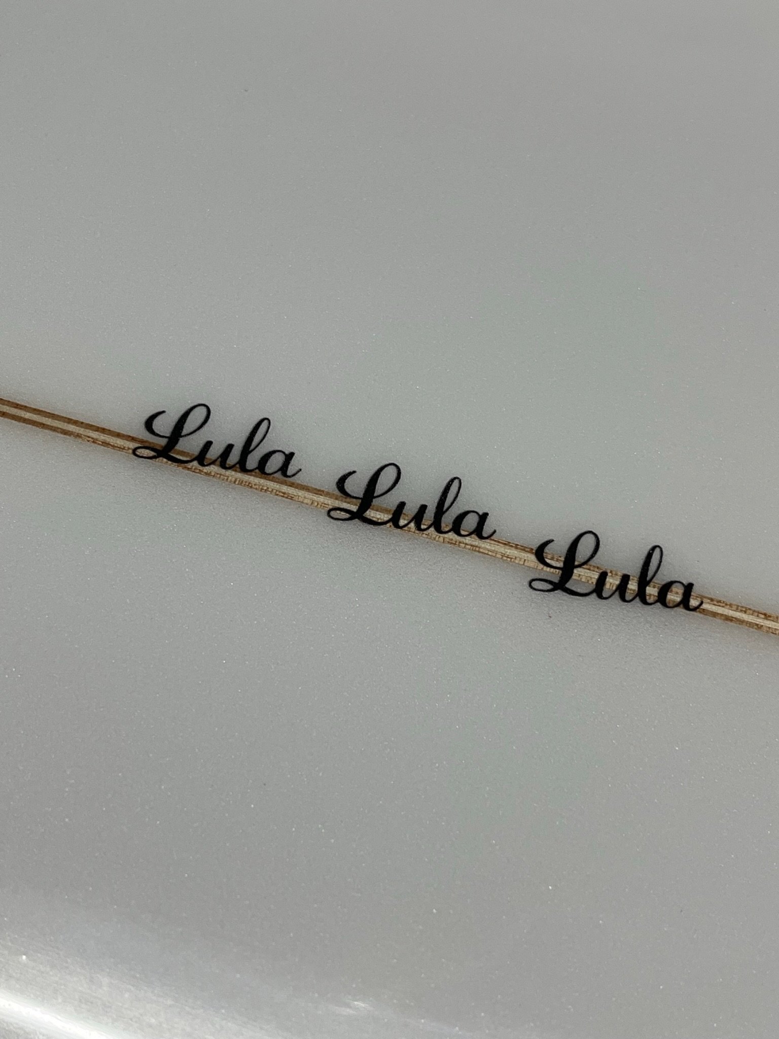 Close-up of a white surface with black cursive text that says "Lula Lula Lula" and surfboard stringer underneath.