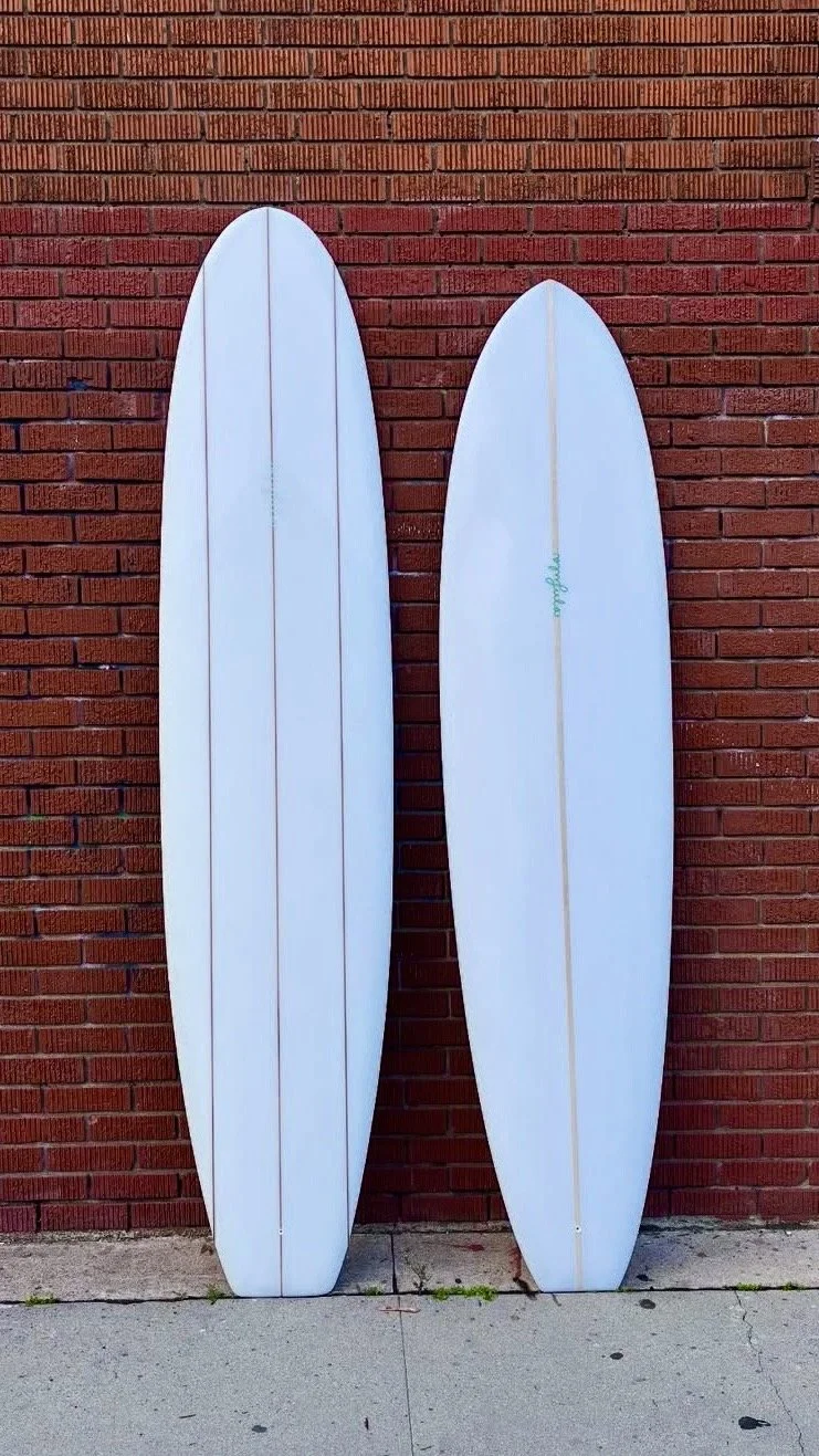 Two white surfboards leaning against a red brick wall on a concrete sidewalk.