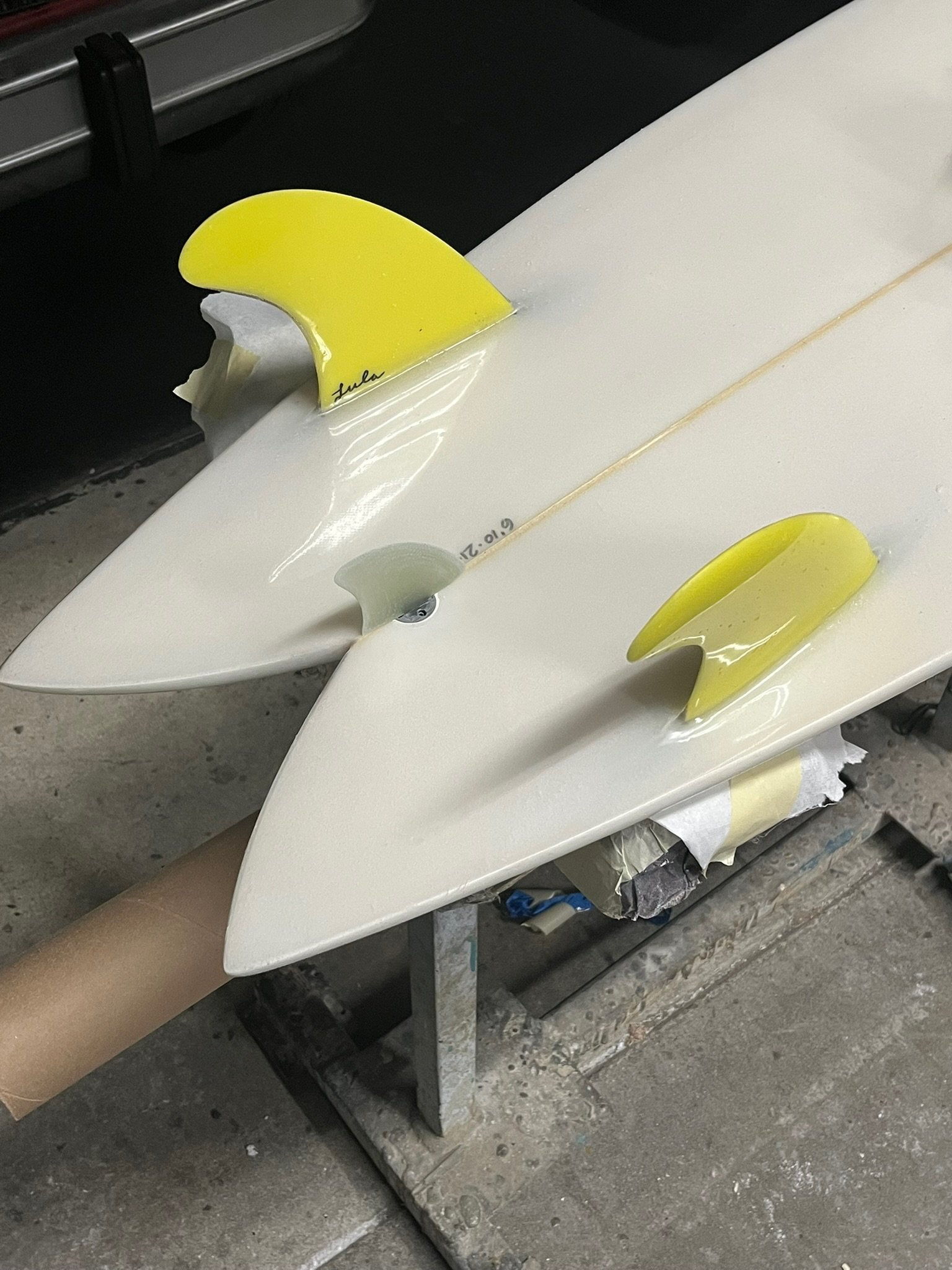 Two surfboards with yellow fins resting on a workbench in a workshop.