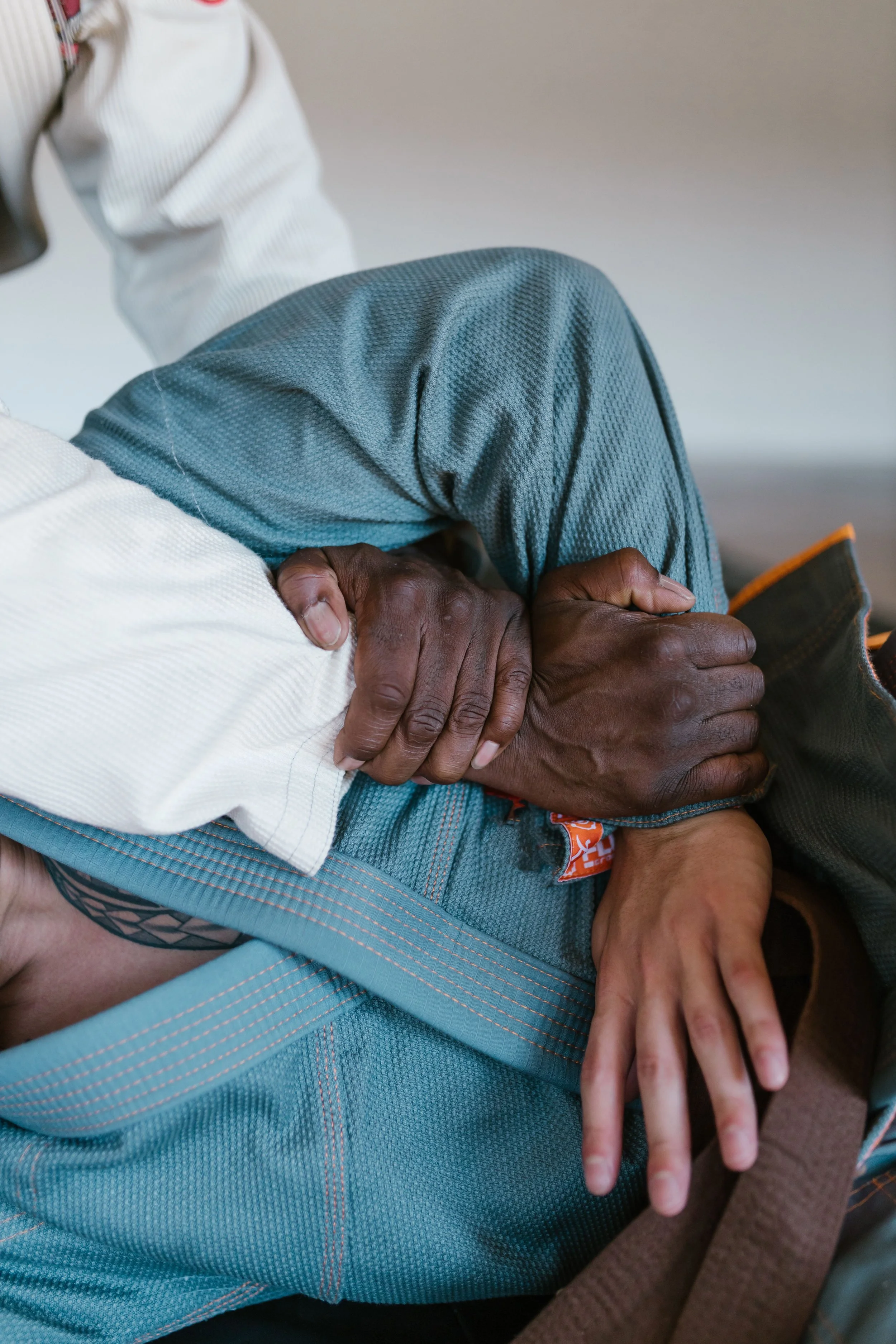 Close-up of a person's hands clasped together, resting on their lap. The person is wearing a white long-sleeve shirt and blue textured shorts. The background is neutral and out of focus.