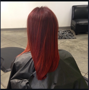 Back view of a woman with straight, long, reddish-brown hair, wearing a black salon cape in a hair salon.