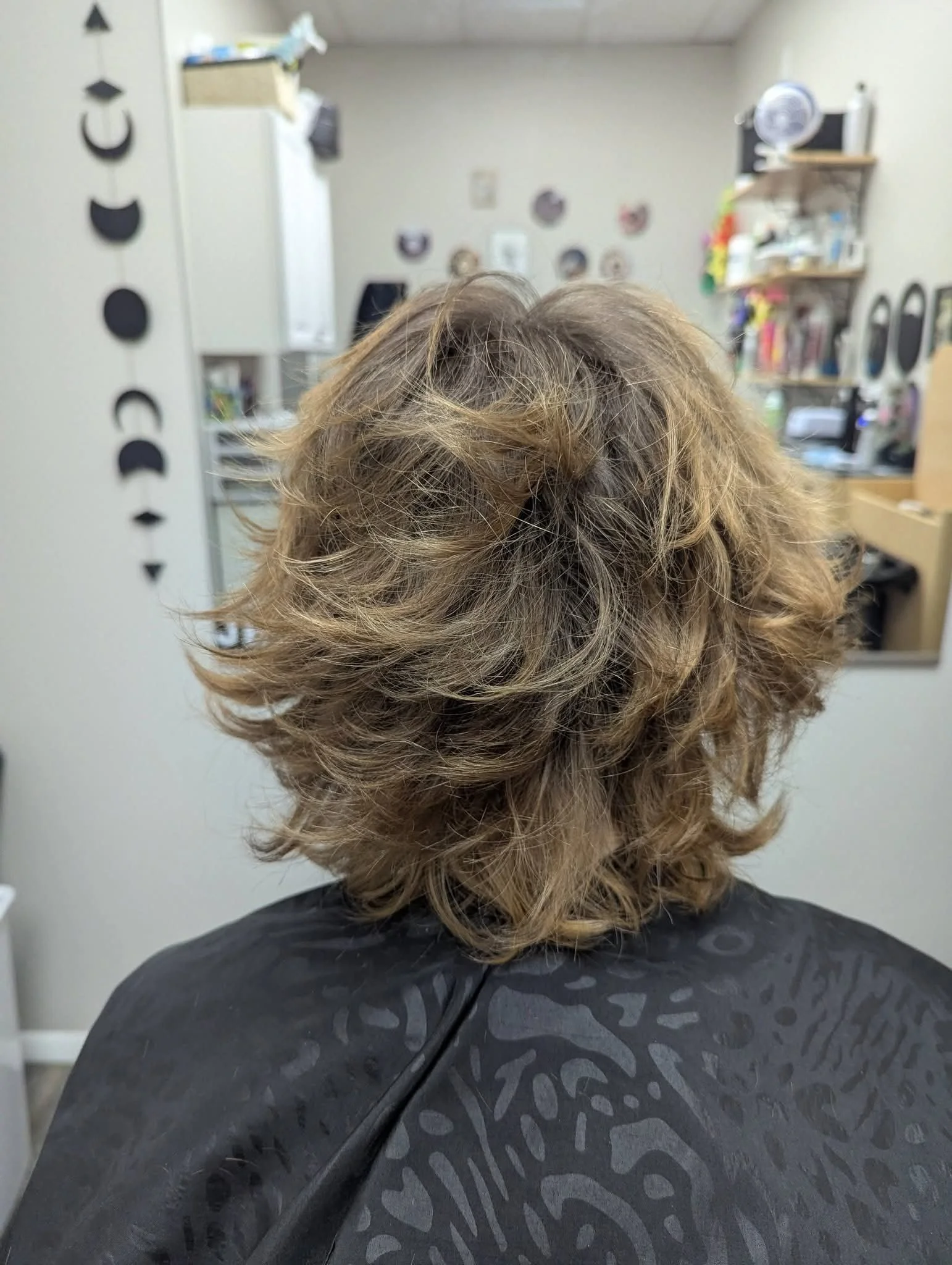 Back of person with curly, light brown hair sitting in a hair salon chair.