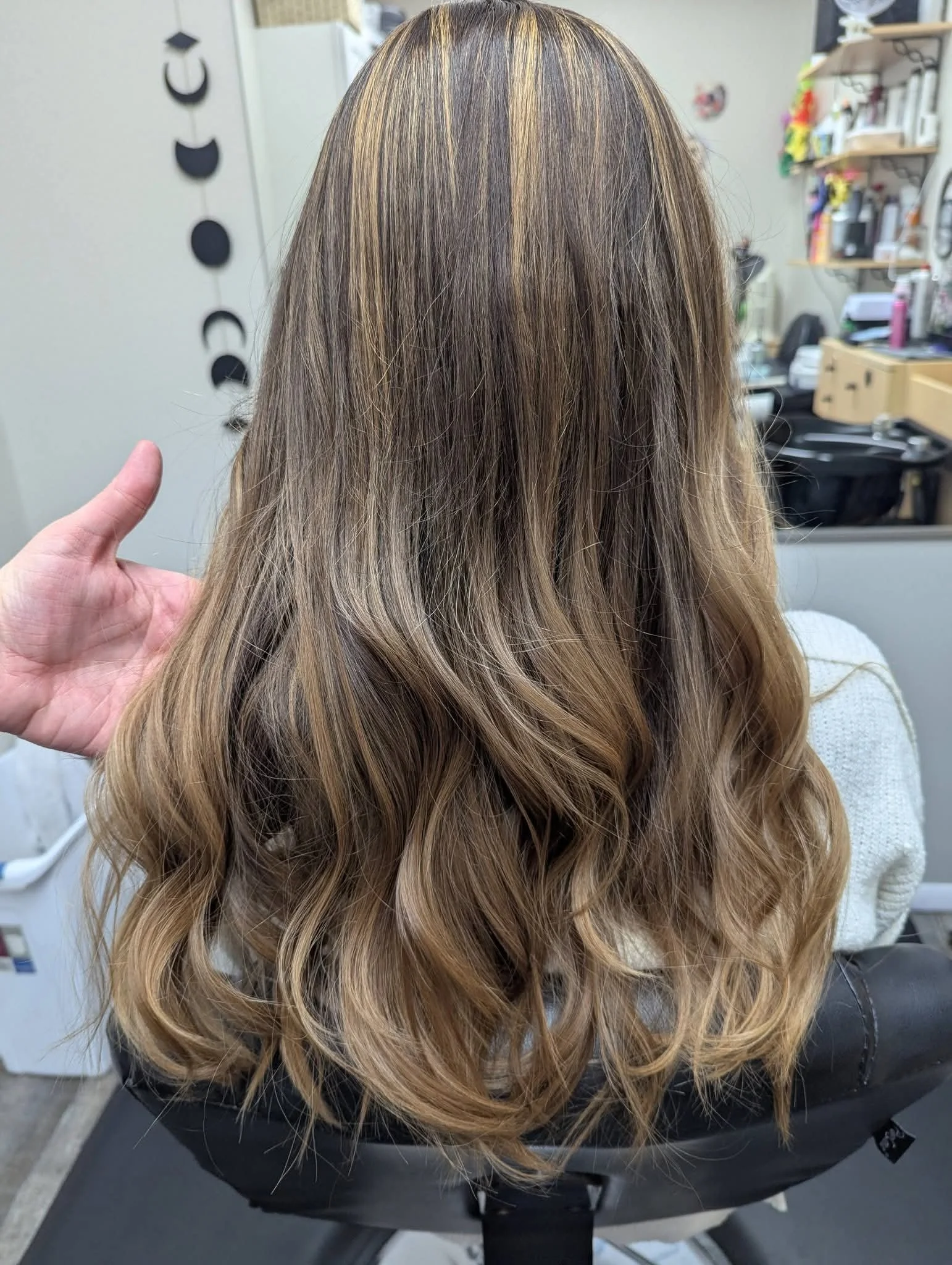 Hair styled with blonde highlights and soft waves, viewed from behind in a salon setting.