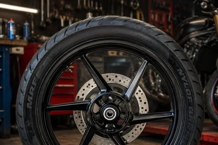 Close-up of a motorcycle wheel with a disc brake, inside a garage or workshop.