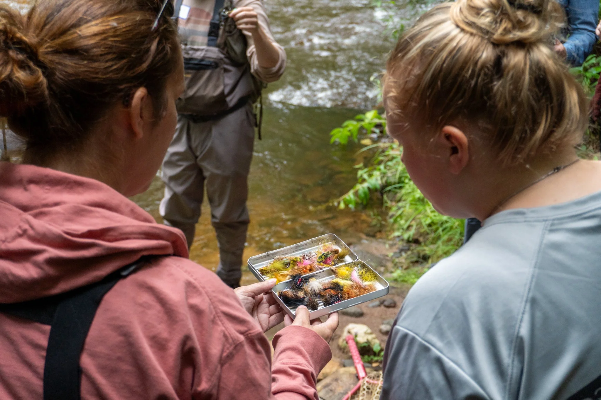 People on a creek bank examining a box of colorful artificial berries.