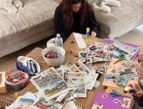 Woman sitting at a table covered with various colorful newspapers and magazines, working on a craft project.