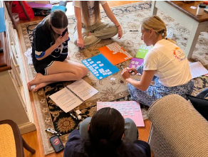 Four children sitting on a carpeted floor playing a board game with colorful cards and paper notes.
