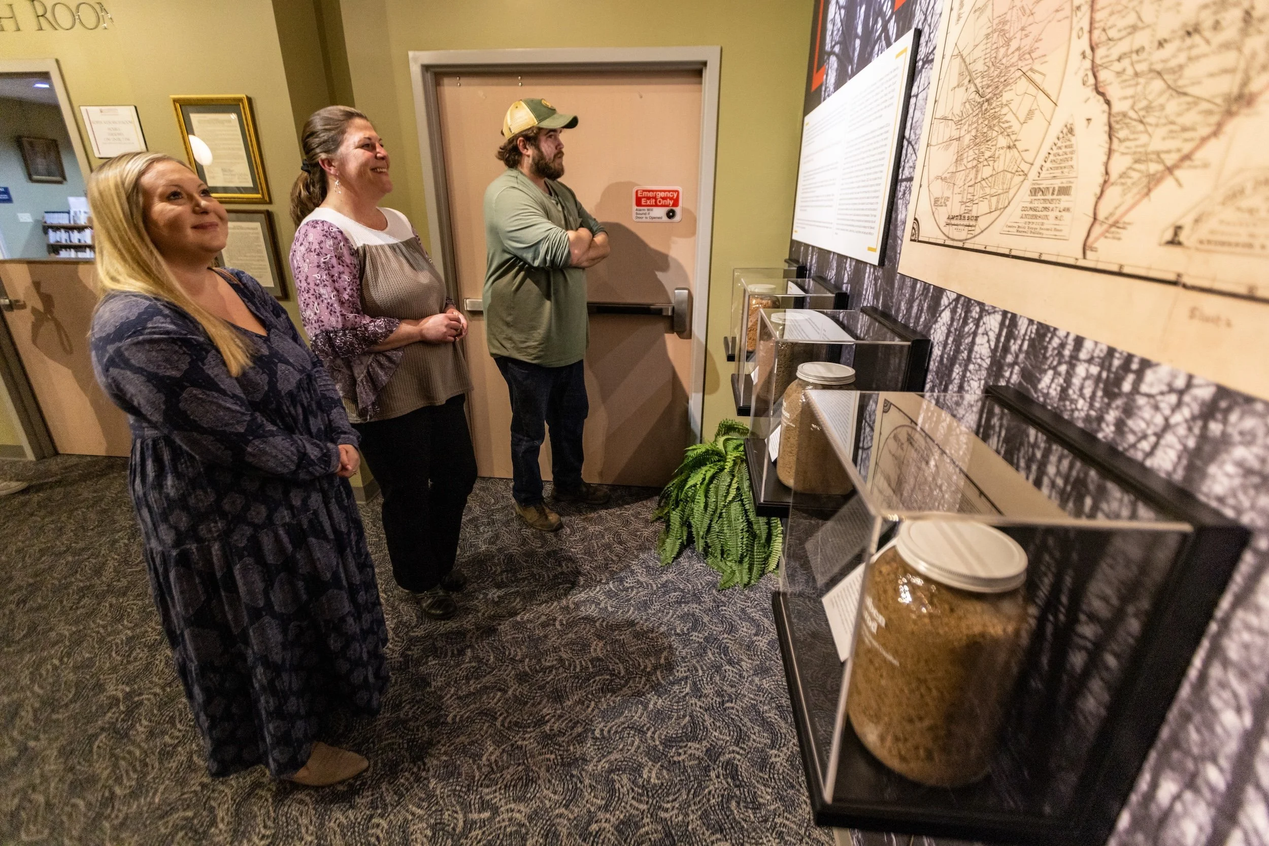 Three women and one man stand in an indoor exhibit, looking at maps and informational displays on the wall.