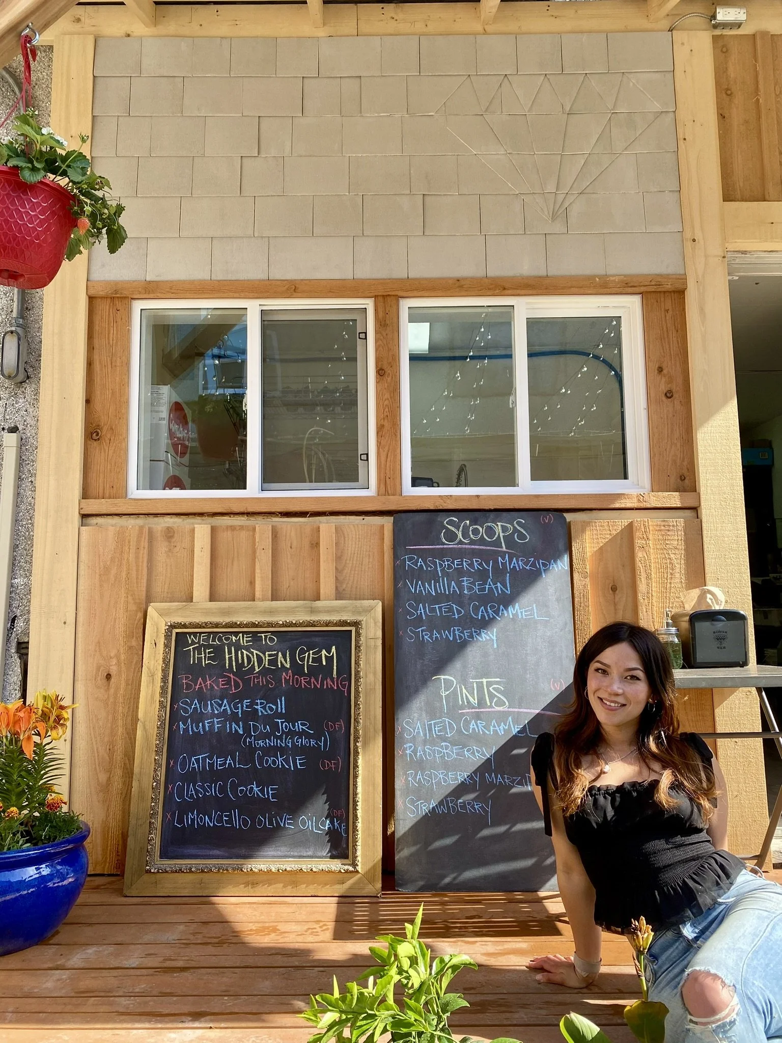 The founder sitting on a wooden deck in front of chalkboards with menu items on opening day and decorative plants nearby.