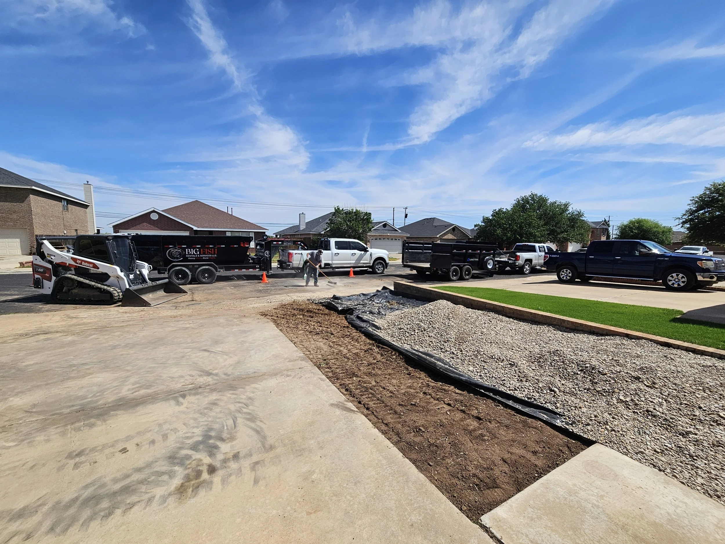 Residential street with houses, trees, and parked trucks, with a partly cloudy sky.