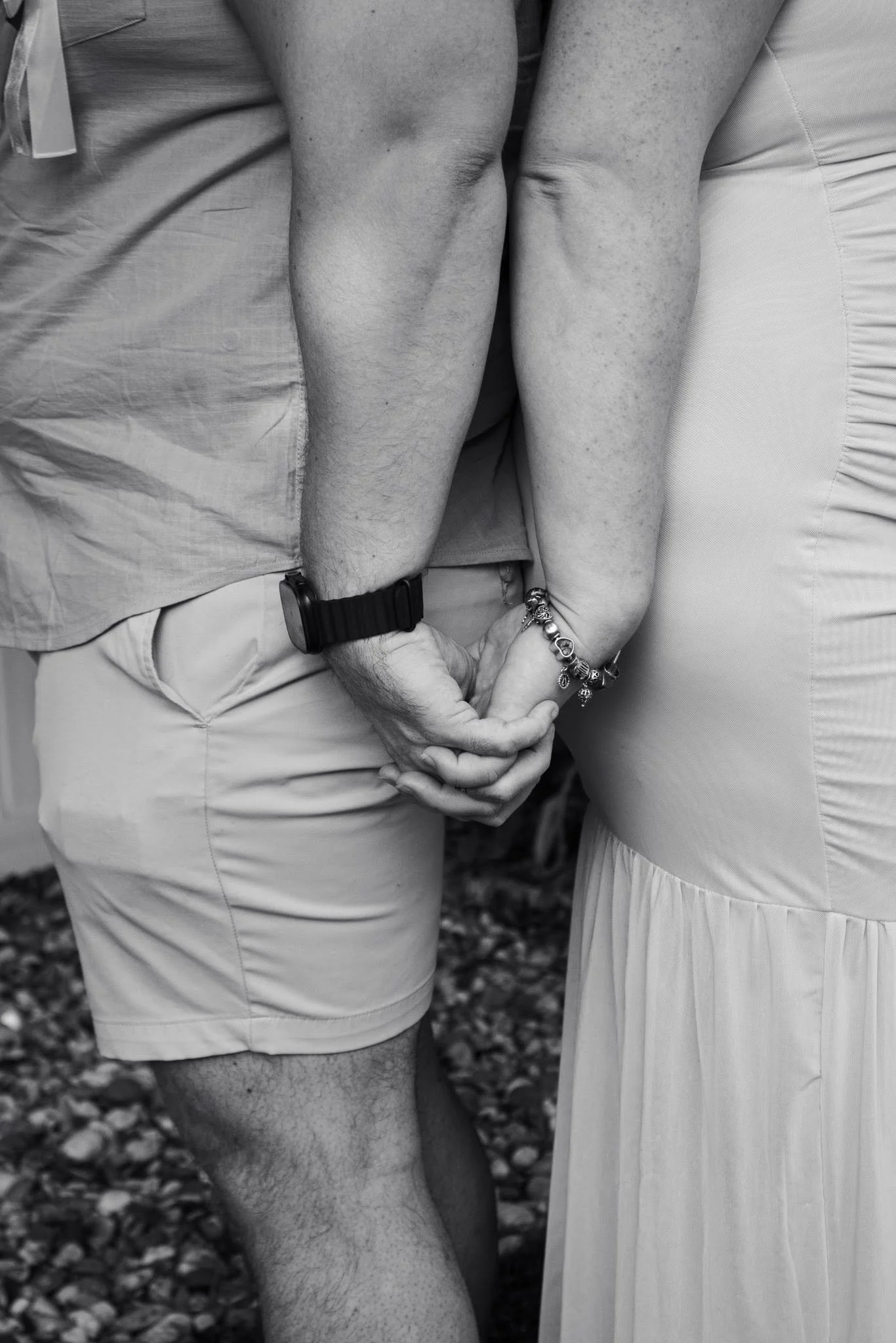 Close-up of a couple holding hands, the man wearing a smartwatch and a bracelet, and the woman wearing a bracelet, standing close together.