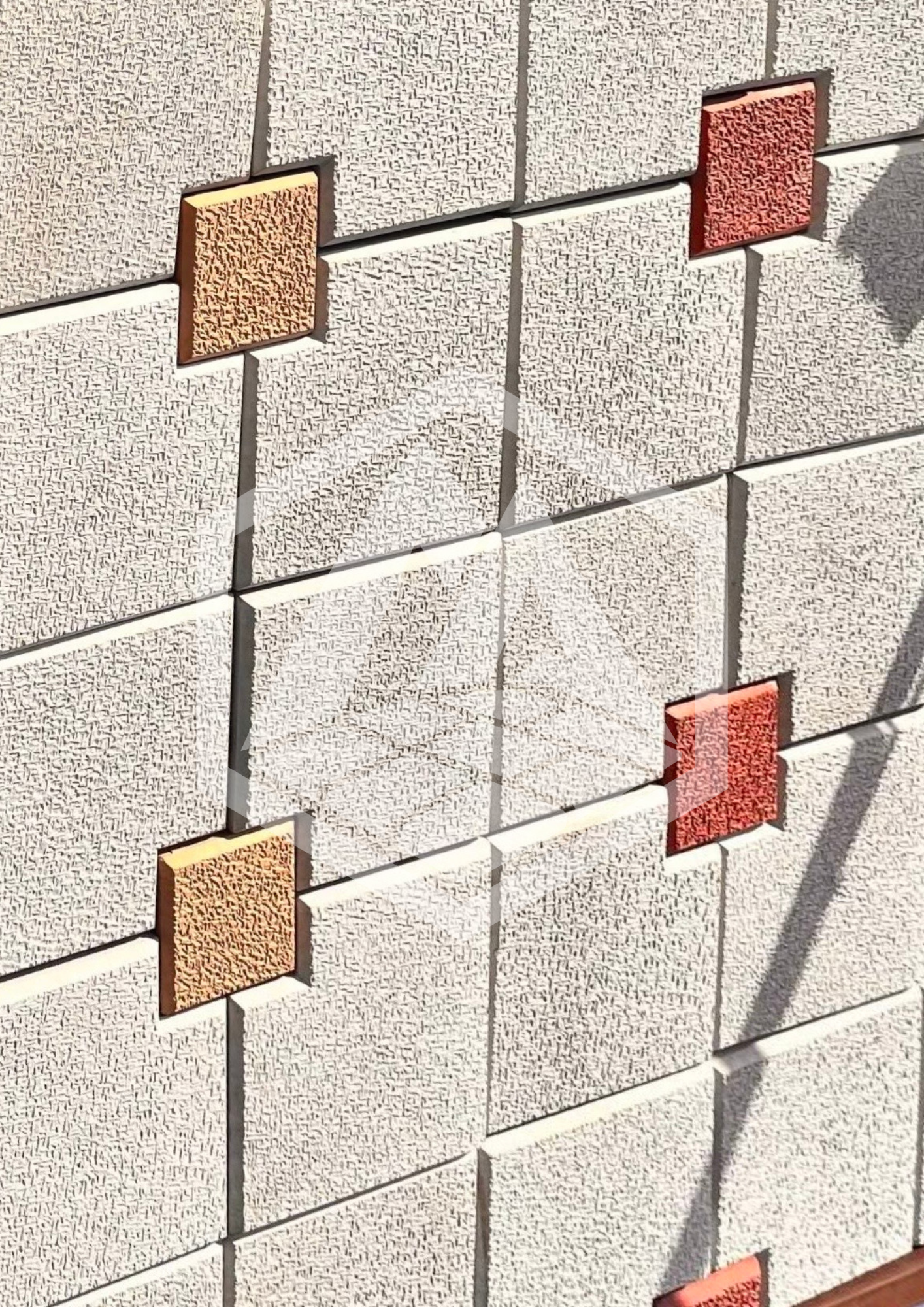 Close-up of a wall with small textured tiles and a few square red and orange tiles arranged on it.