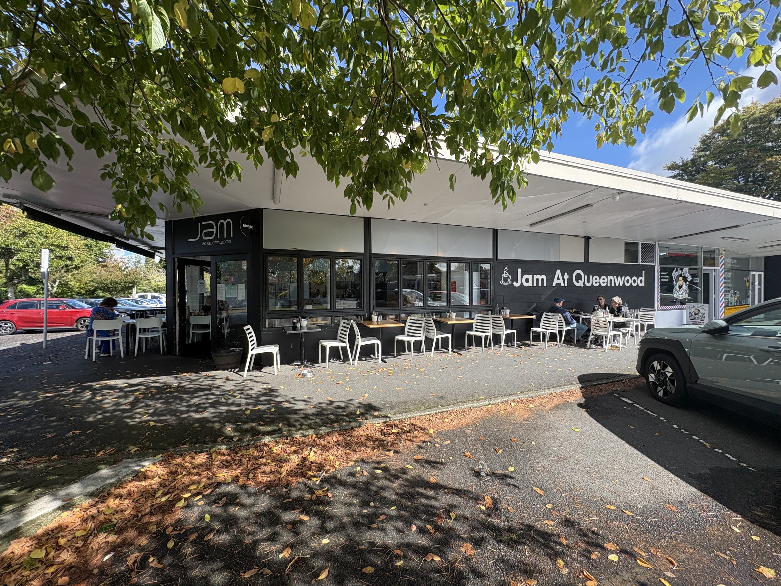 Exterior view of Jam at Queenwood restaurant with outdoor seating area, trees, parked cars, and a blue sky