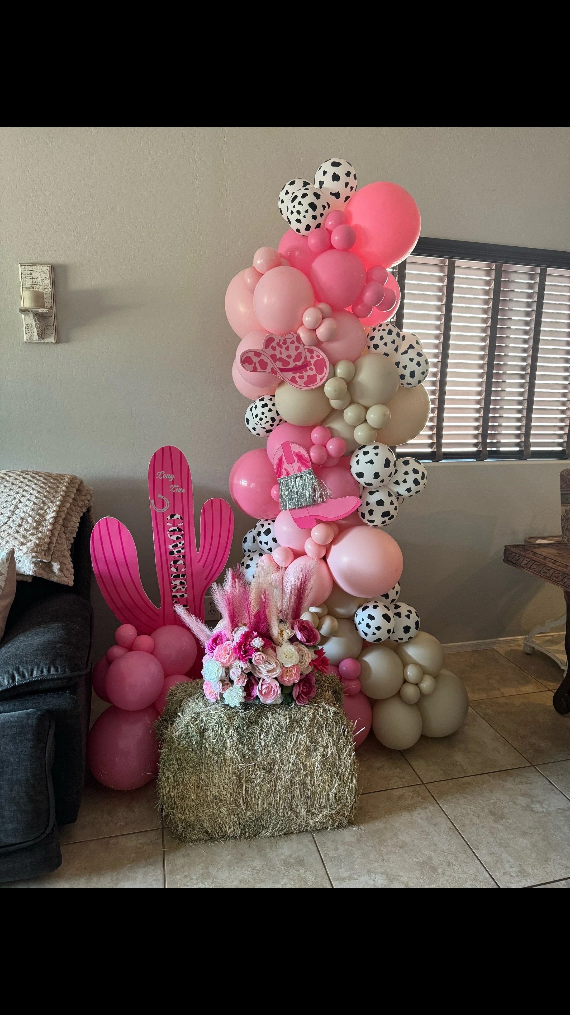 Long Live Cowgirls! freestanding balloon garland for this cowgirl's birthday surprise featuring pink balloons, cow print balloons, cactus & hay bale props