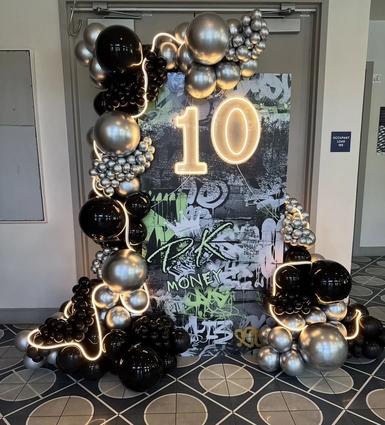 Y2k club vibes for this birthday celebration featuring a custom graffiti backdrop, LED number sign & ropes, Black and Silver Balloons