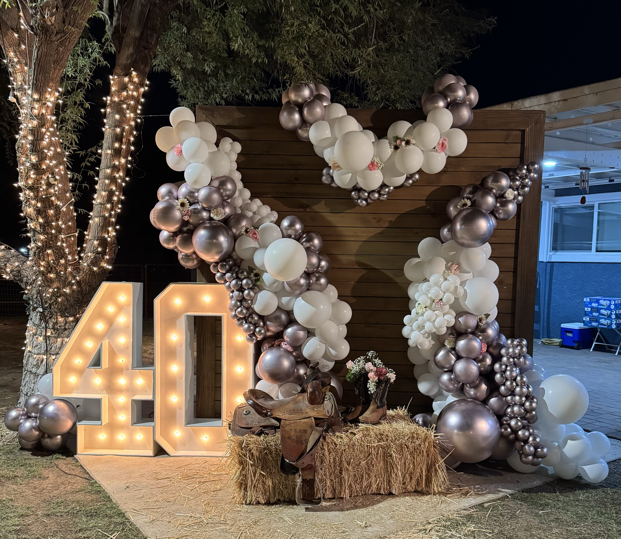 Western Birthday party featuring Pink Chrome and White Balloons, western backdrop, marquee numbers, hay bale & horse sattle accents