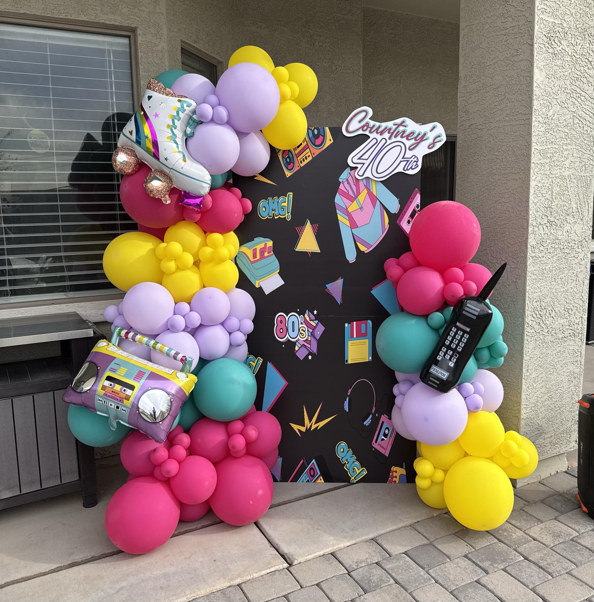 80's themed custom backdrop with colorful balloons & retro phone, boombox and roller-skate accents for this 40th birthday celebration