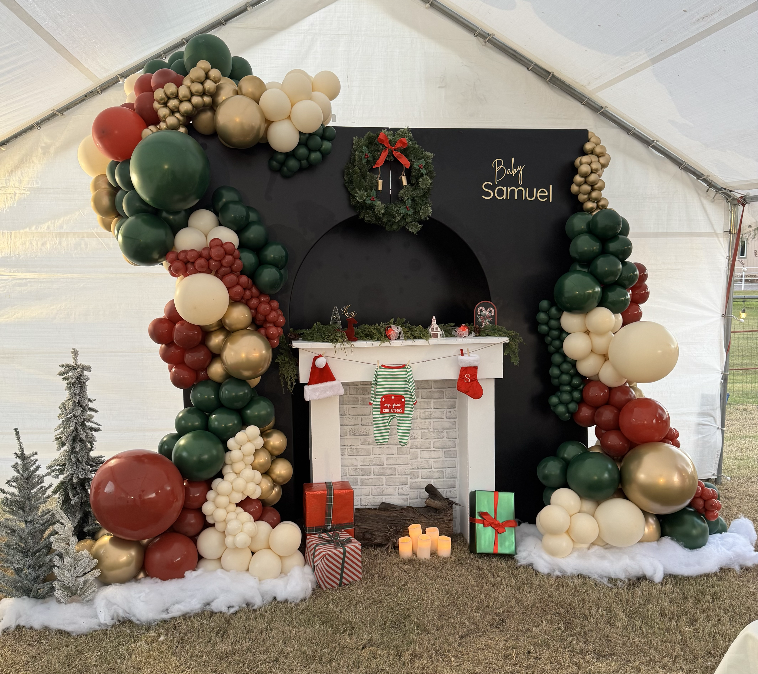 Christmas themed baby shower celebration featuring a custom Fireplace prop, gifts, Christmas trees, snow, and a 3D backdrop. Red, green, gold & cream balloons