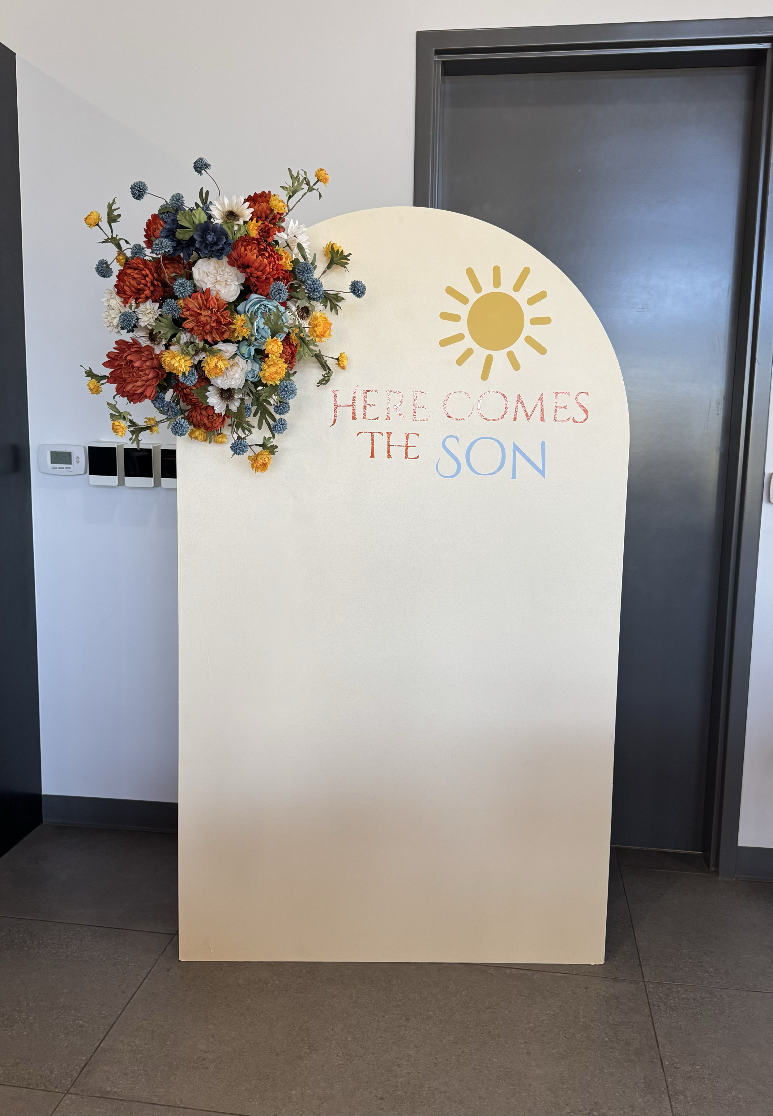 'Here Comes the SON' baby shower backdrop and floral arrangement