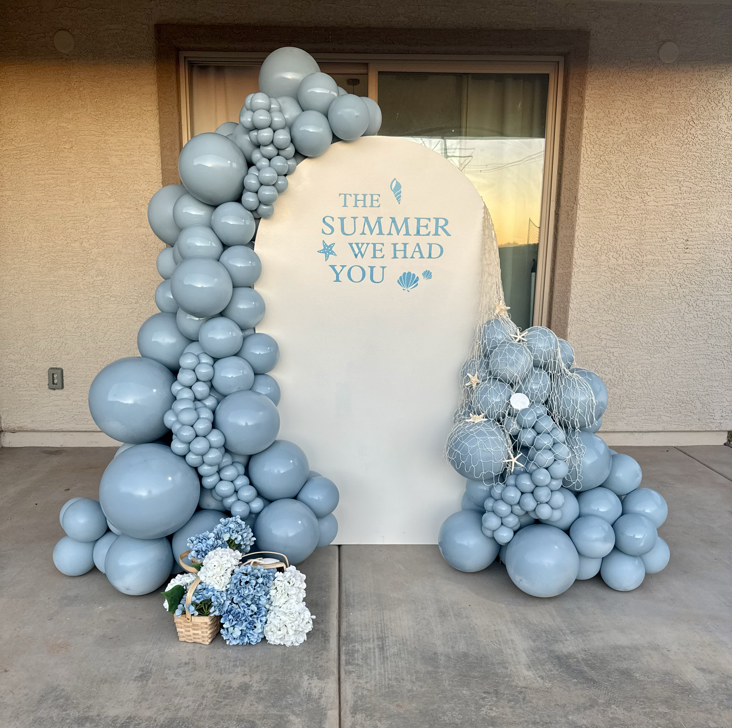 "The Summer We Had You" Coastal Vibes featuring monochromatic light blue balloons, seashells, fish net, and baskets with blue and white flowers. Perfect baby shower theme for fans of the show 'The Summer I Turned Pretty'