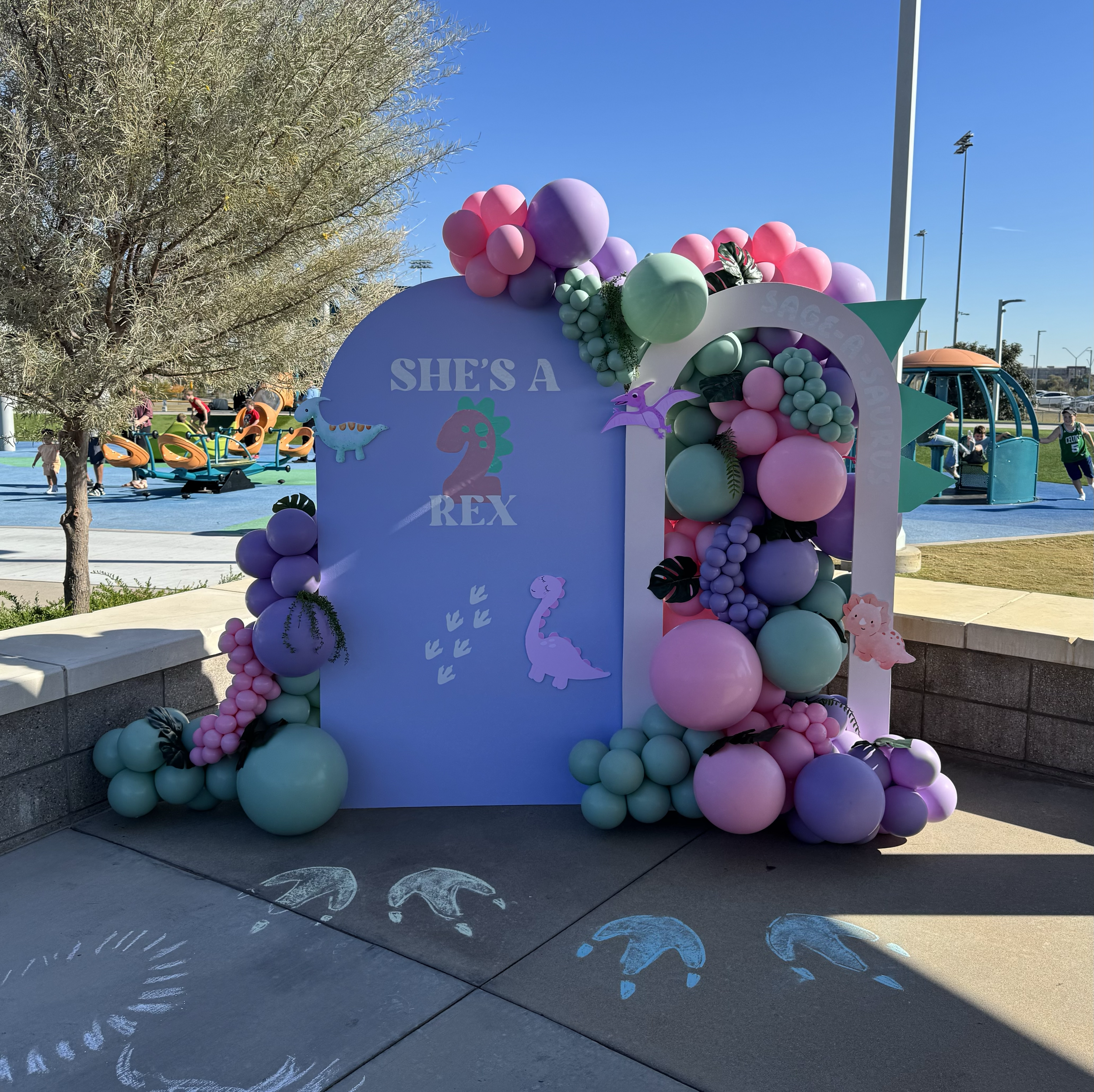 "She's a 2Rex!" Girly dinosaur birthday setup with small Dino cutouts, greenery accents, and pink, purple & green balloons