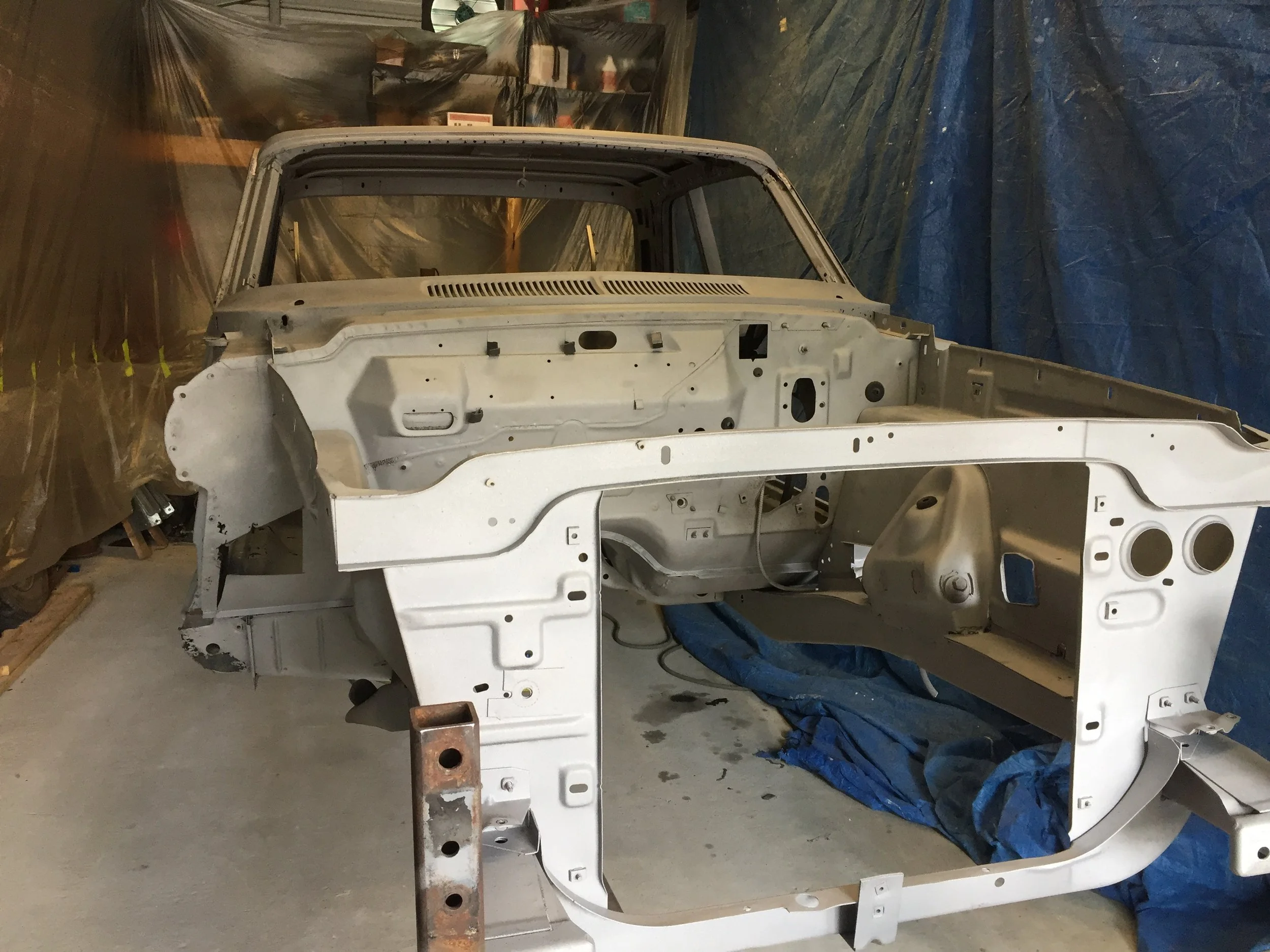 A white car body shell in a garage or workshop with plastic sheeting and tools around it.
