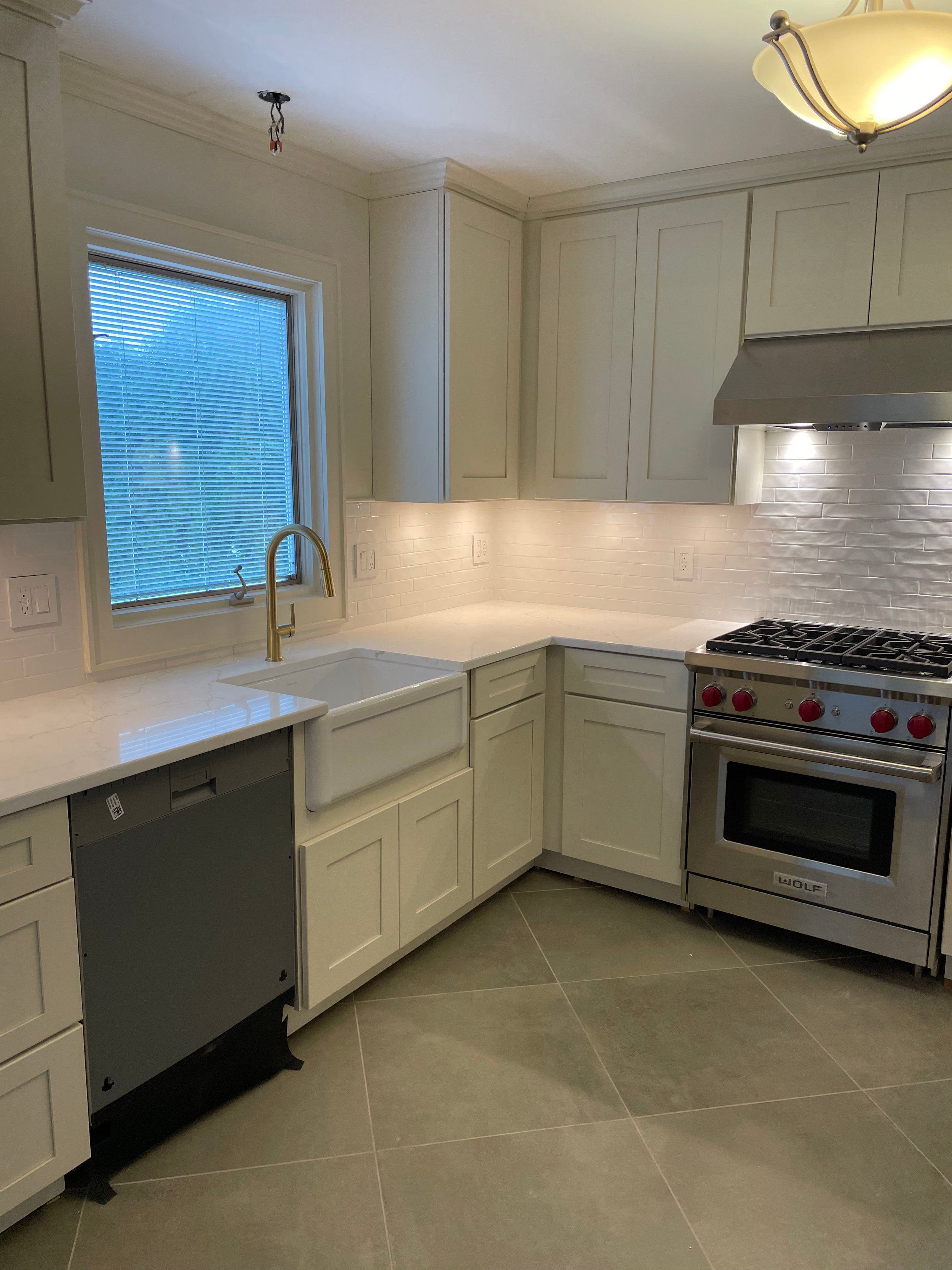 Newly renovated kitchen with white cabinets, stainless steel oven, and tile backsplash, no ceiling light fixture installed yet.