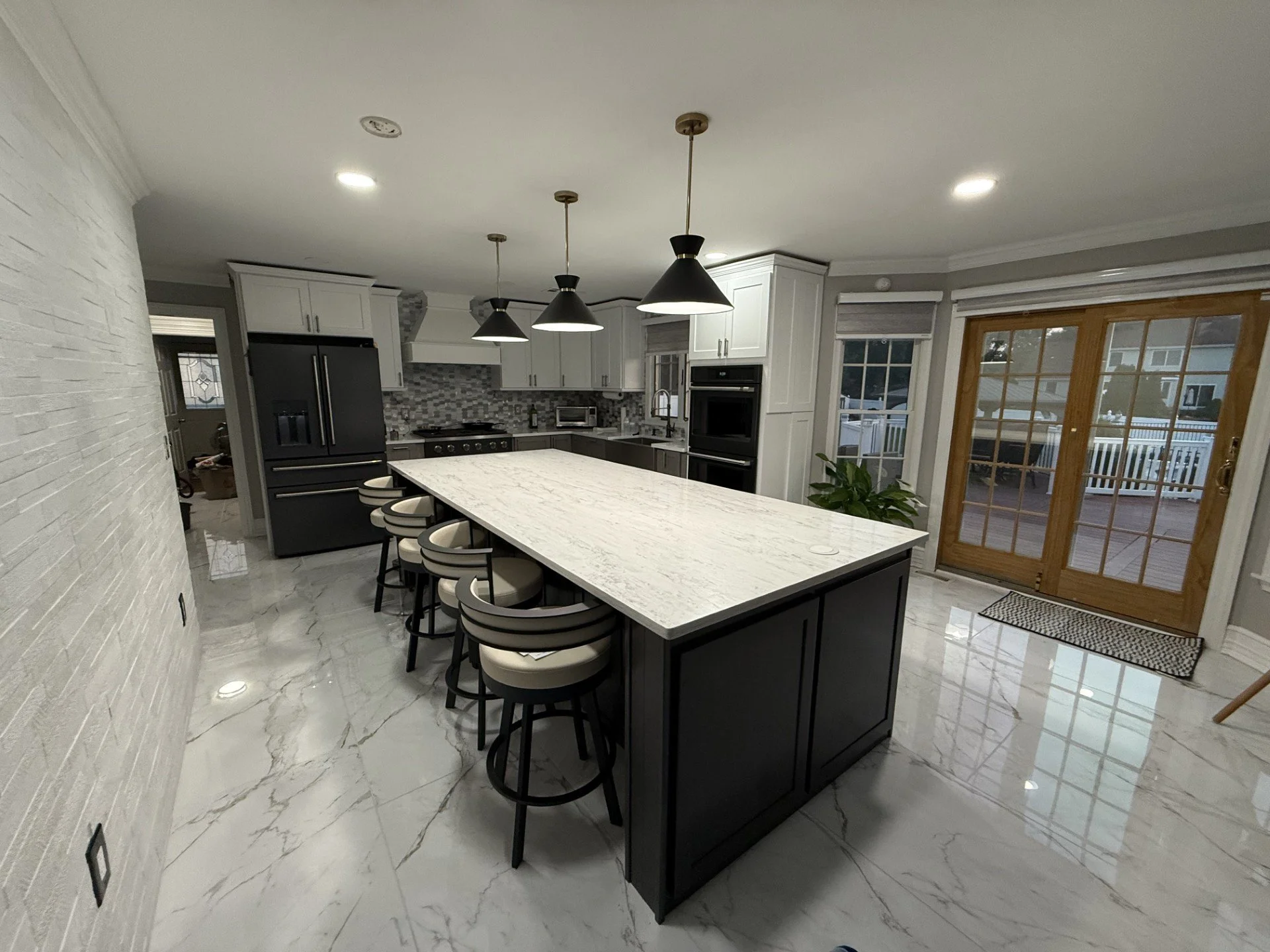 Modern kitchen with white cabinets, gray backsplash, black appliances, marble island, and sliding glass door leading outside.