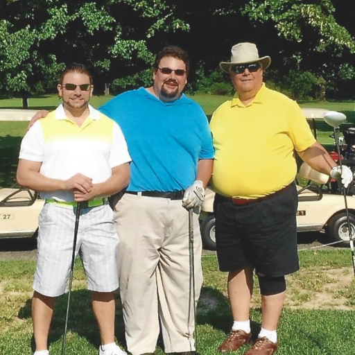 Three men standing on a golf course with golf carts in the background, holding golf clubs, dressed in casual golf attire.