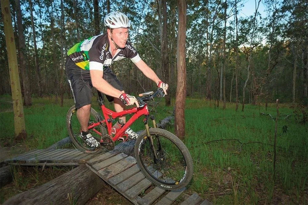 Person mountain biking on a wooden trail in a forest.