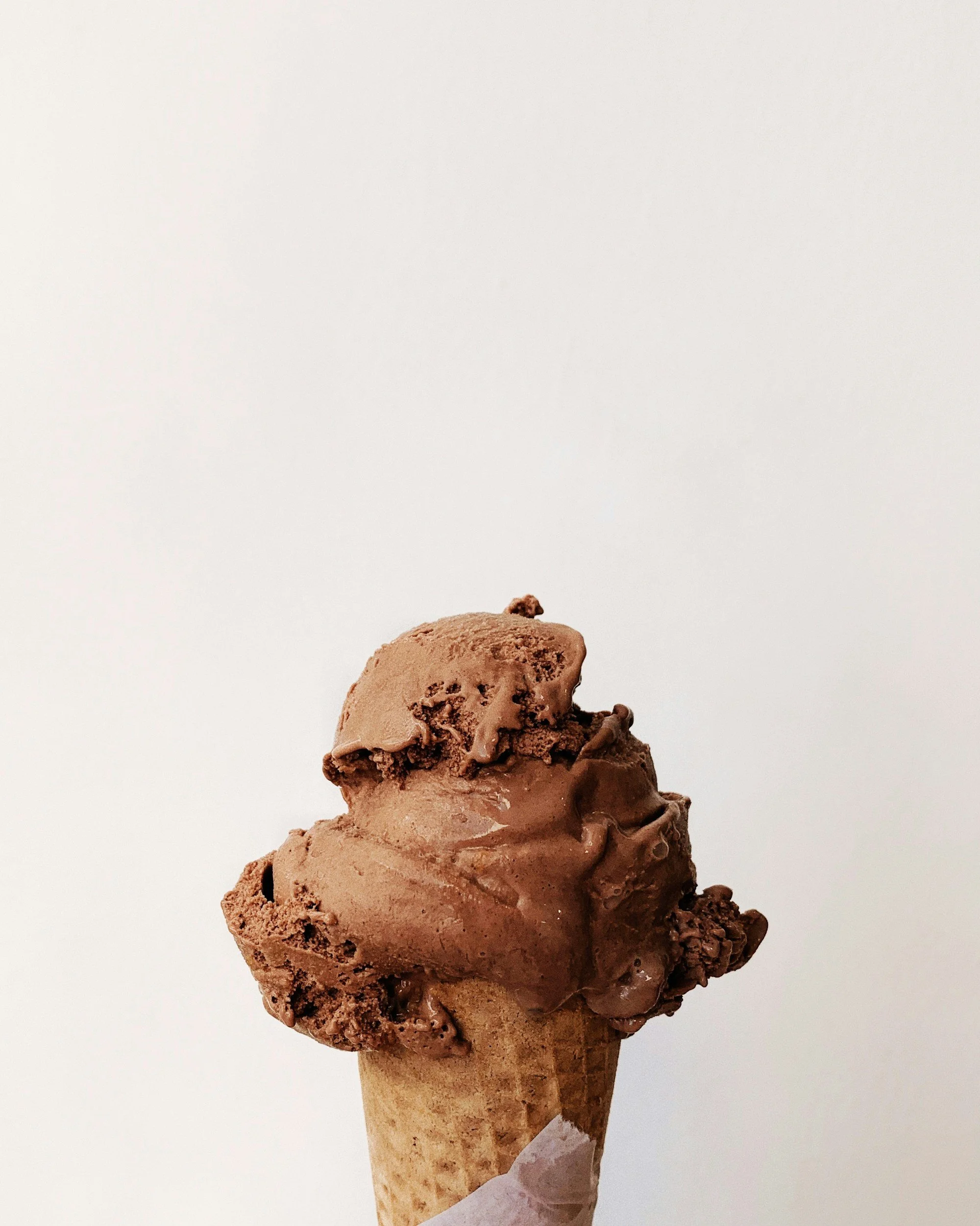 A close-up of a triple scoop chocolate ice cream cone with a plain white background.
