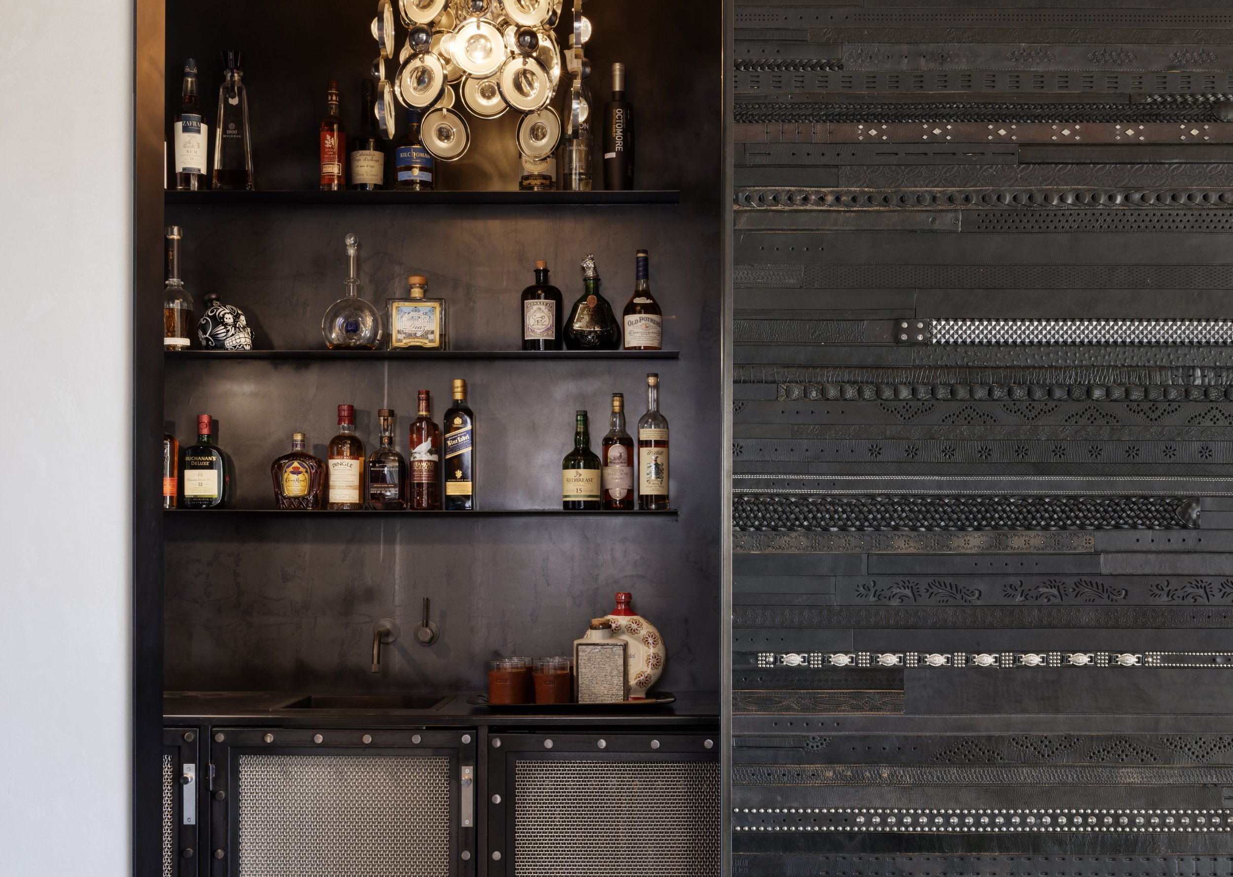 A bar shelf displaying assorted liquor bottles and a skull-shaped decorative item, set against a dark wall with modern textured paneling.