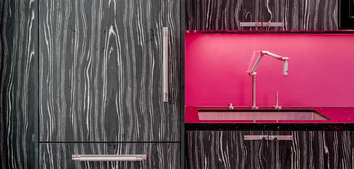 A modern kitchen with dark gray and black striped cabinets, a pink backsplash, and a pink countertop with a sink and a flexible faucet.