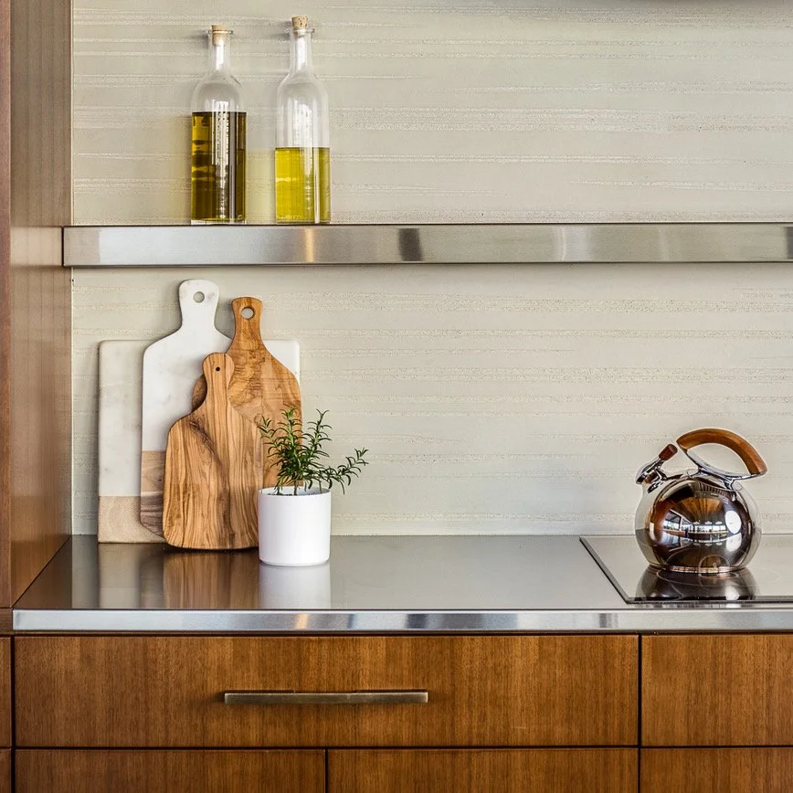 Kitchen counter with two oil bottles, cutting boards, a potted plant, and a tea kettle.